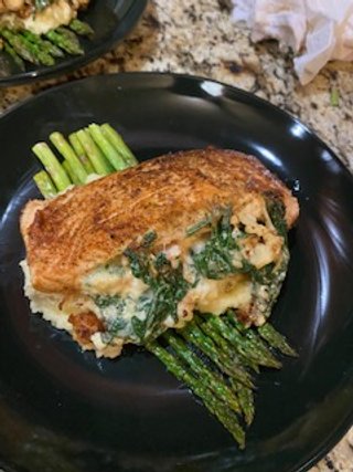 Baked salmon fillet with asparagus spears on a black plate.