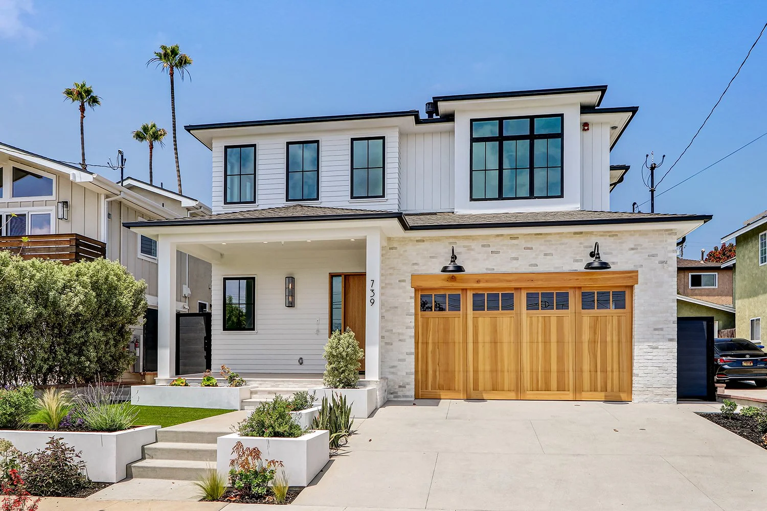 Modern two-story house with a stone and siding exterior, large windows, a covered porch, landscaped front yard, and a two-car garage.