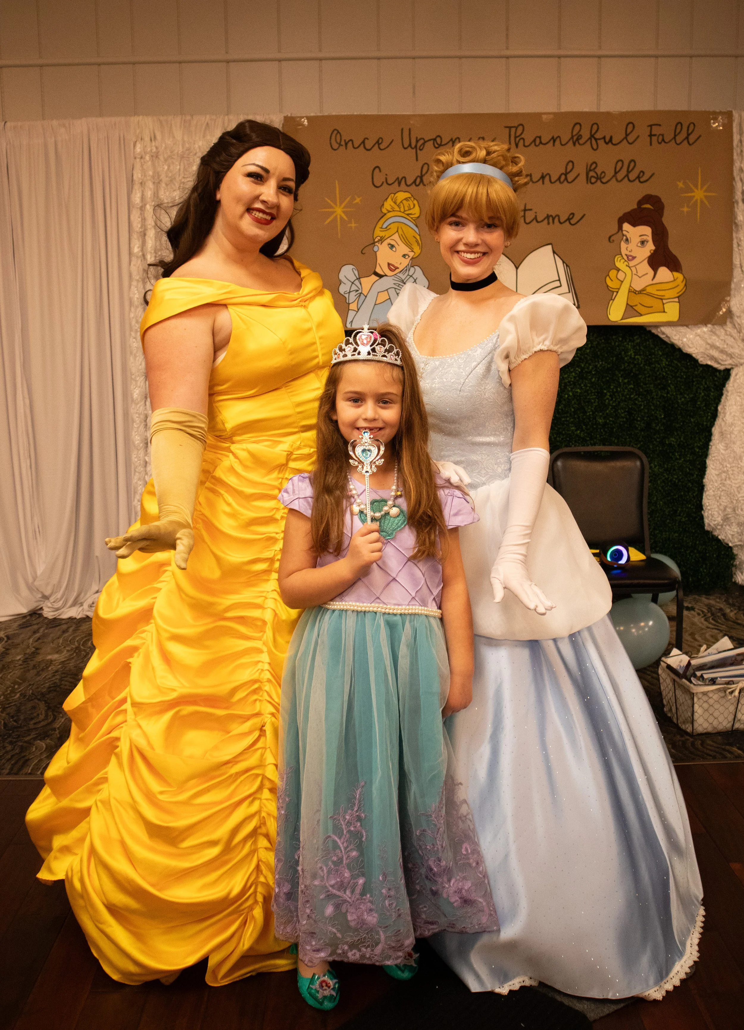 A decorated dining table set for a bridal shower with place settings, mimosas, glasses of water, a centerpiece with white roses, and gifts in the background, in a cozy room with fairy lights.