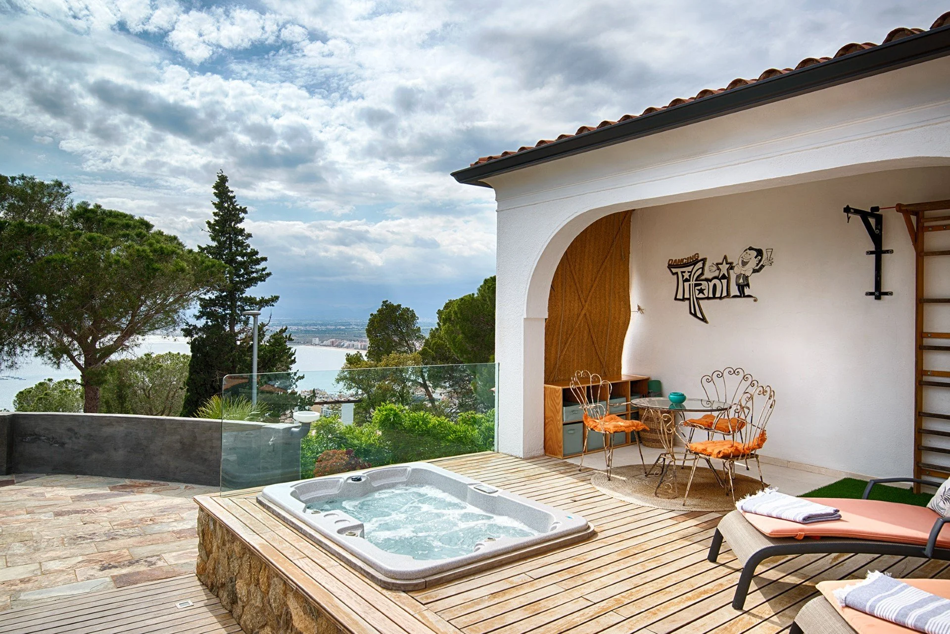 Outdoor patio with hot tub, lounge chairs, a dining area, and a view of trees and sky