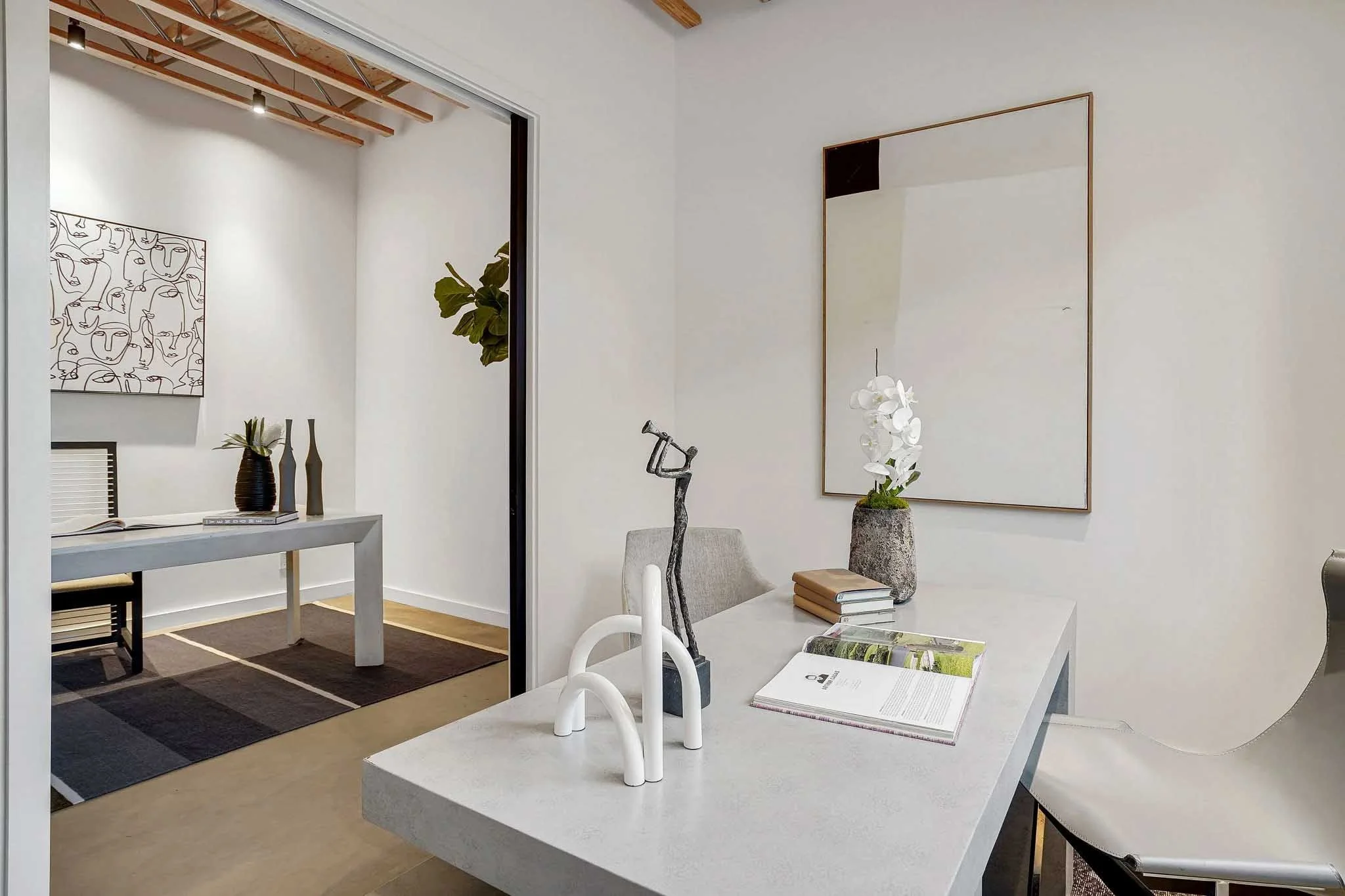 Modern interior of a home office with a white desk, decorative items, and a large mirror on the wall.
