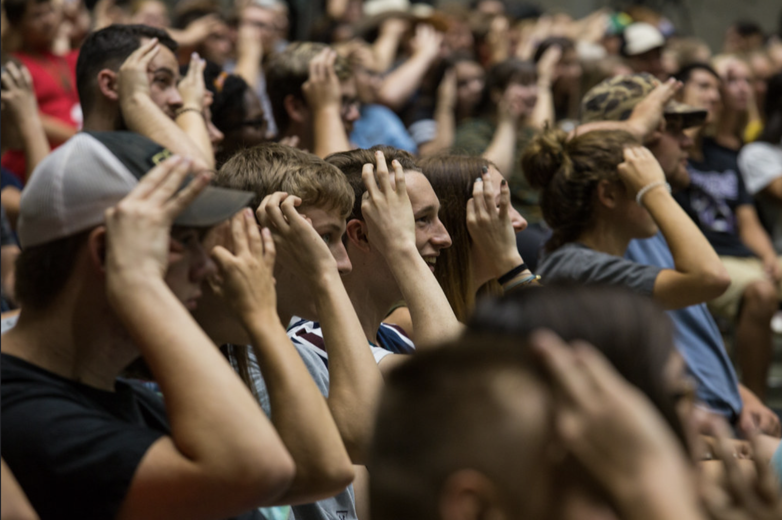 Audience members seated in a large indoor auditorium, covering their ears, watching an event with expressions of surprise and focus.