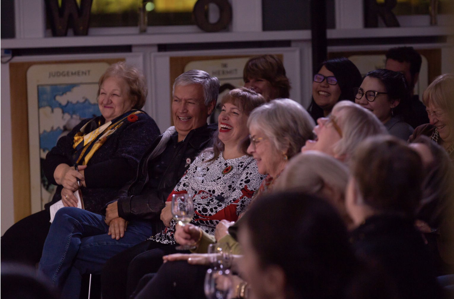 A group of diverse adults sitting in a row, laughing and enjoying a public event.
