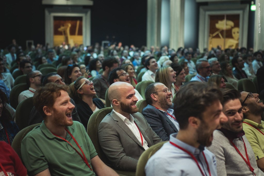 Audience at a conference or event, sitting in a theater or auditorium, laughing and enjoying a presentation.