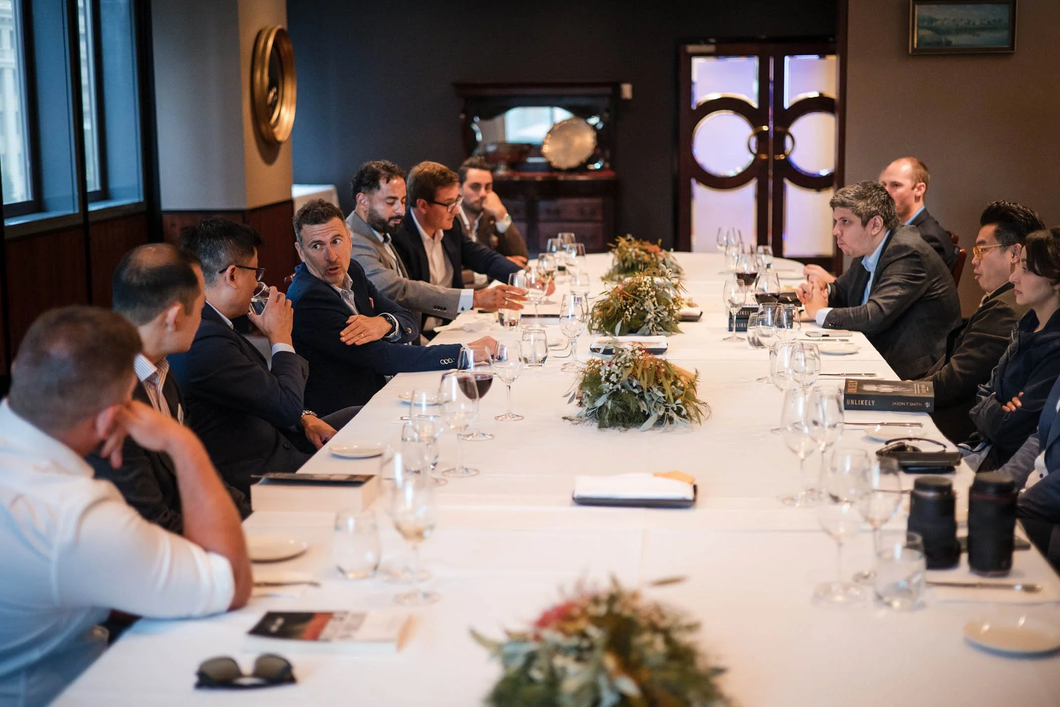 Business meeting with executives seated around a long table in a formal conference room.