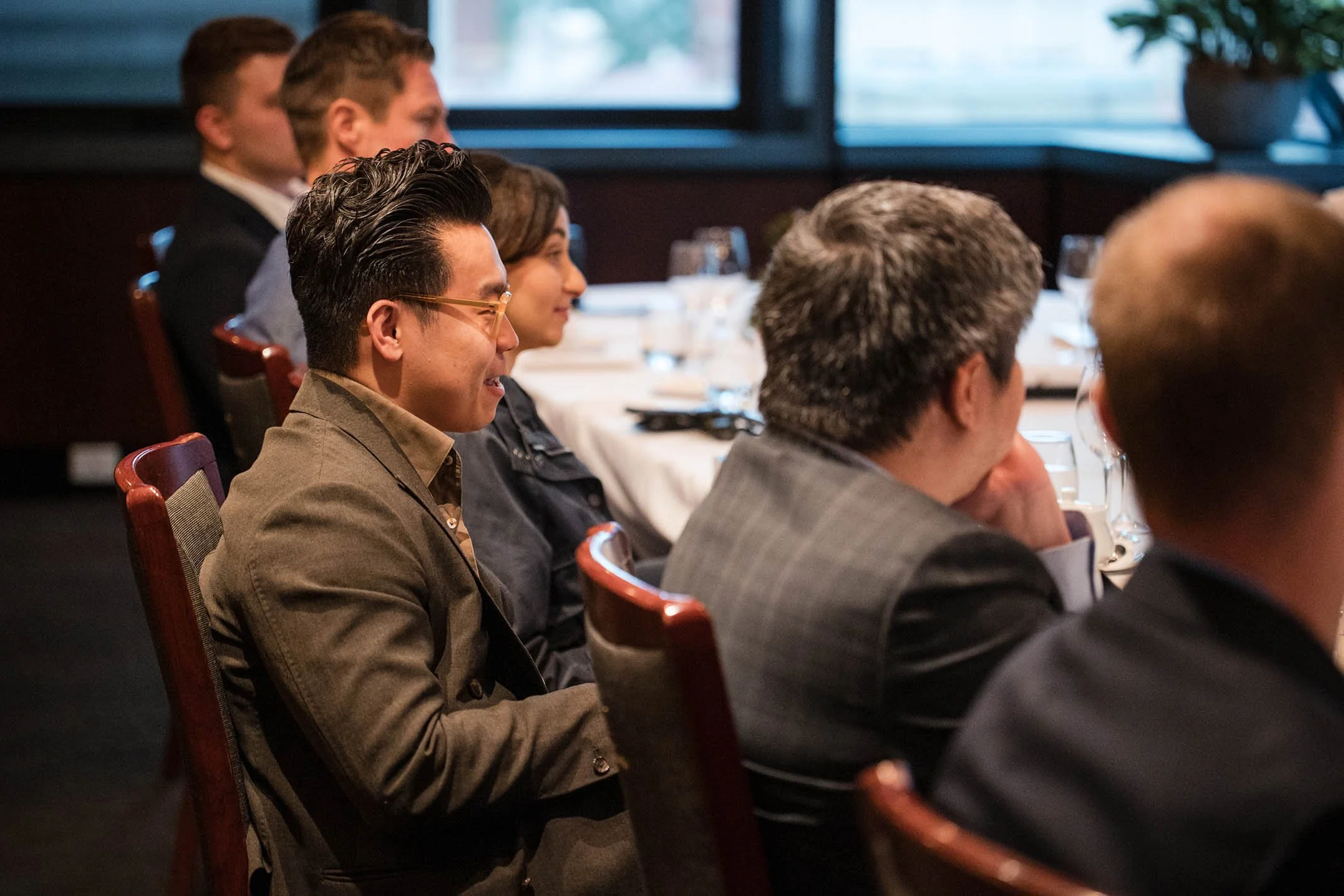 People sitting at a dinner table attending a formal event in a restaurant or conference room, dressed in business attire.