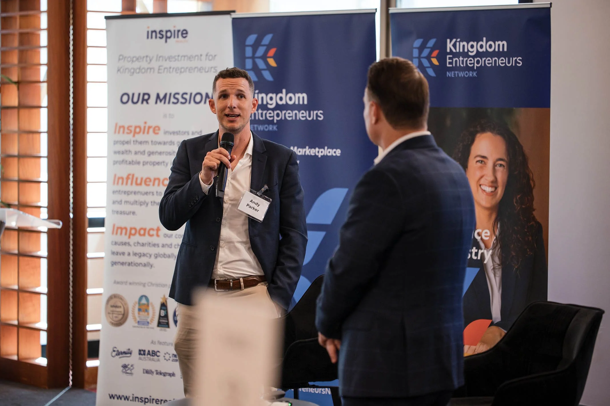 A man with a microphone speaking to another man at a networking event with Kingdom Entrepreneurs banners in the background.
