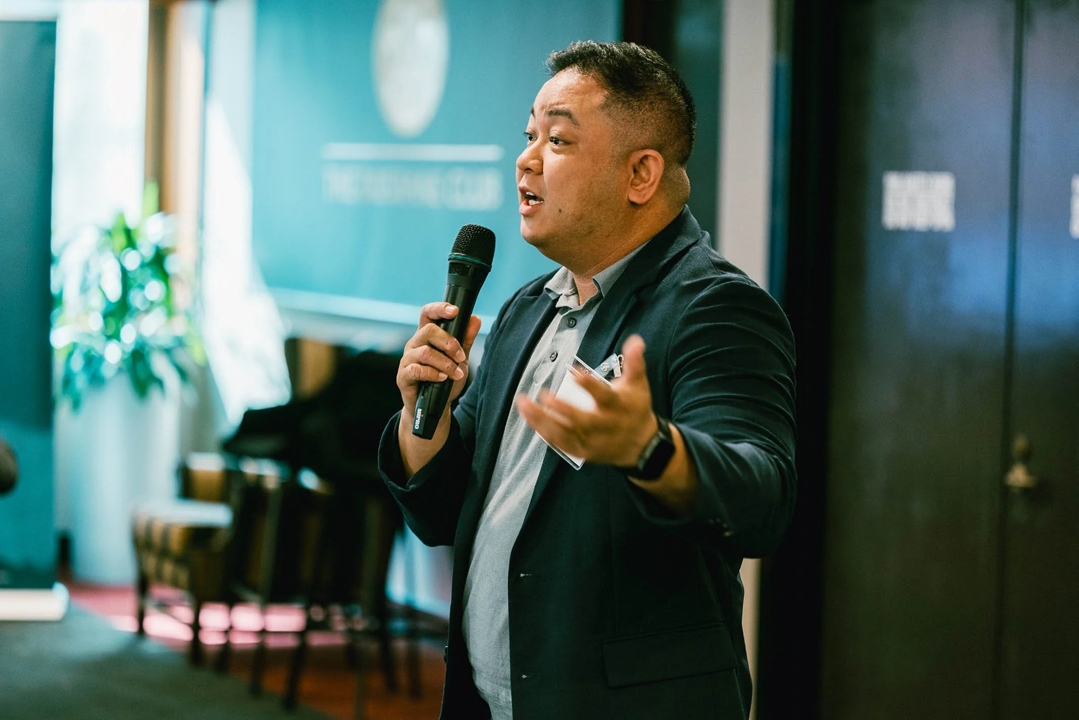 A man speaking into a microphone during a presentation or speech in a conference room.