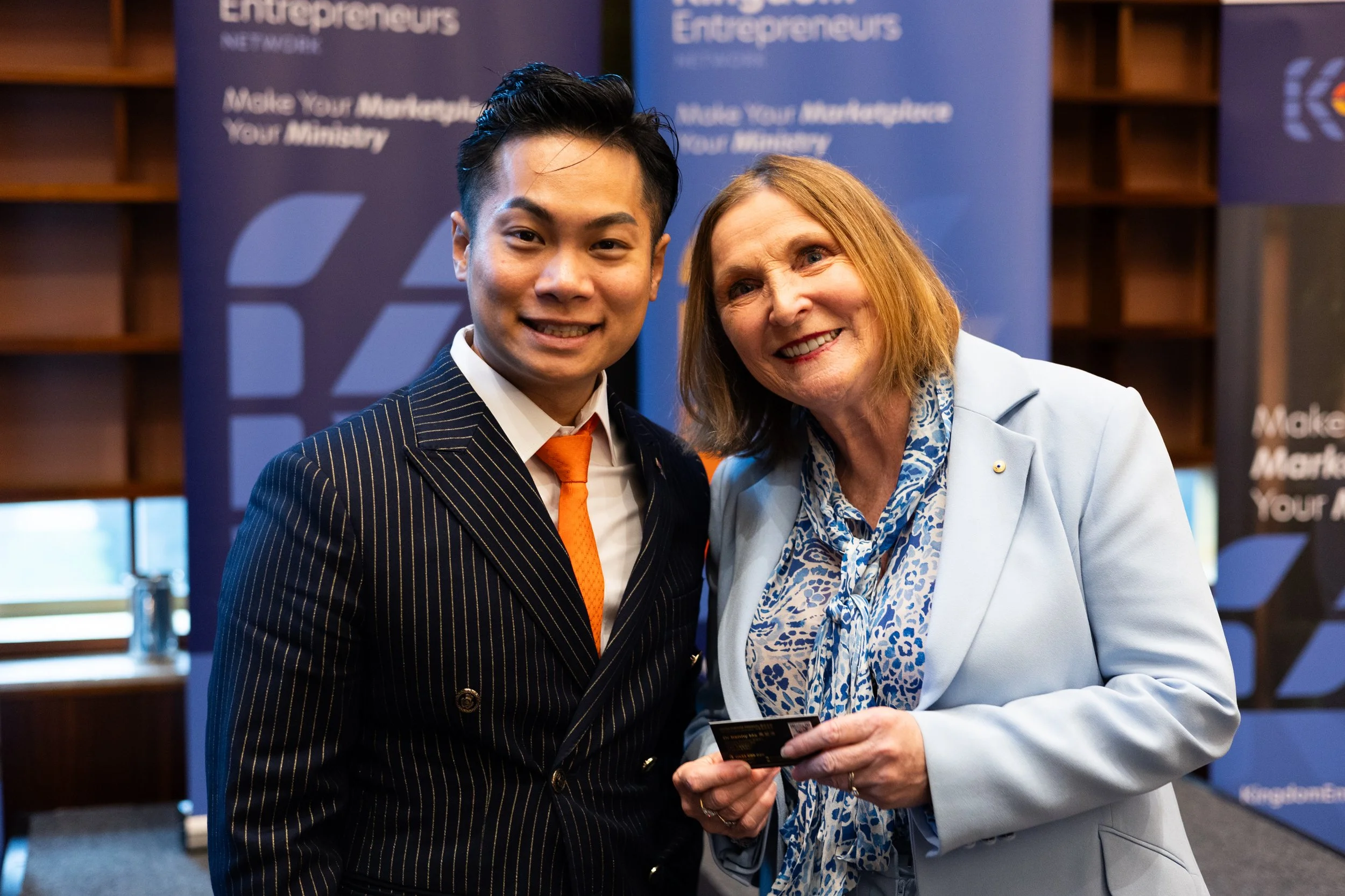 Two women smiling at a professional event, standing in front of banners that read 'Entrepreneurs' and 'Make Your Marketplace Your Ministry'.