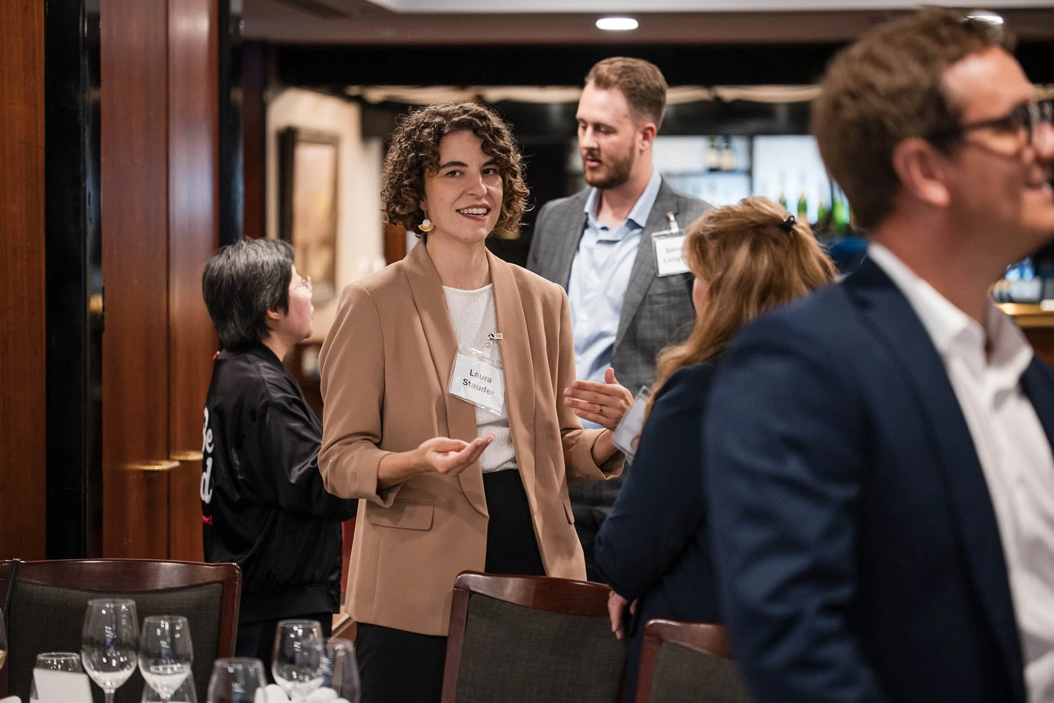 A woman with curly hair talking to a group of people at a networking event in a restaurant or hotel setting.