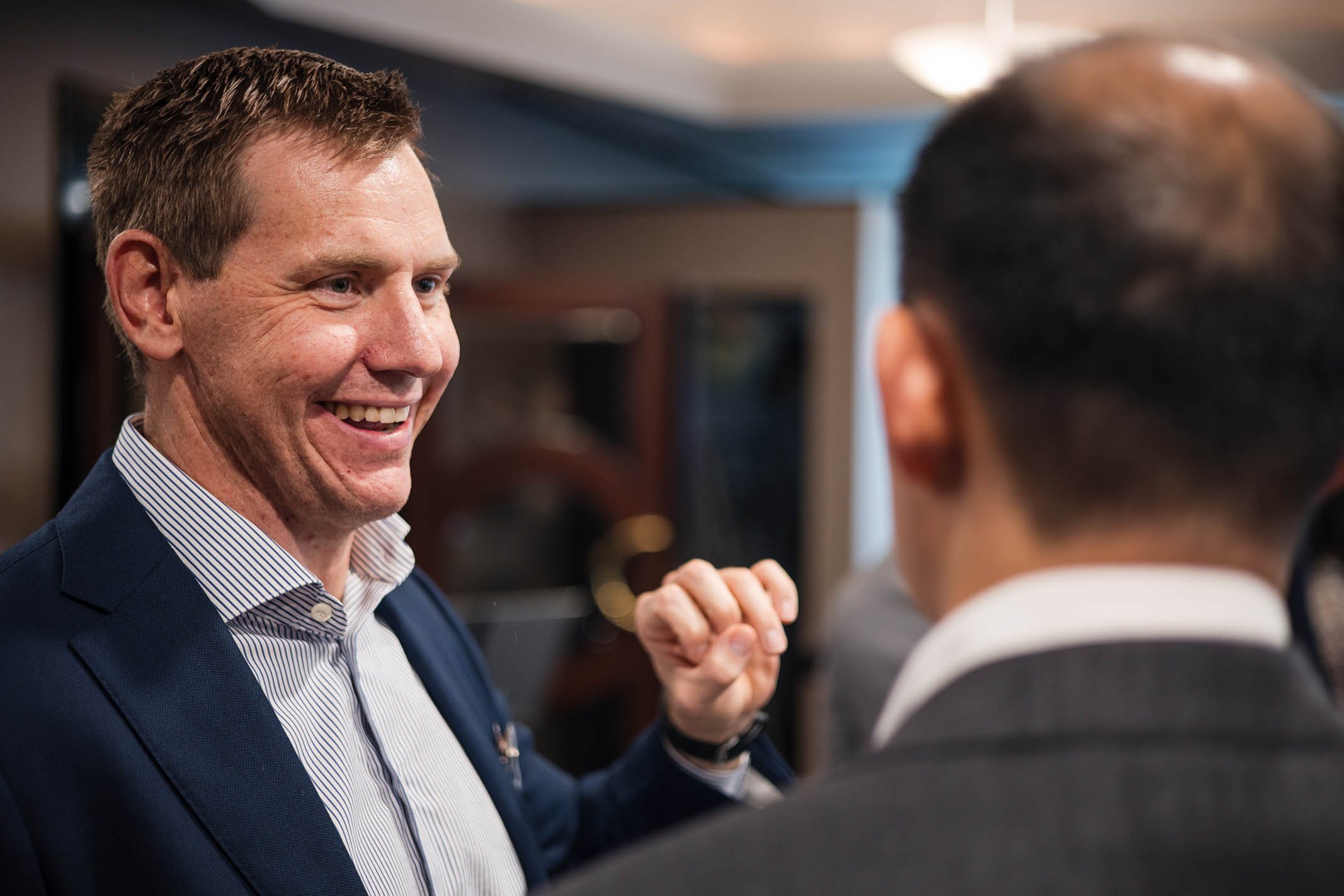 Two men in business suits smiling and exchanging a fist bump in an indoor setting.