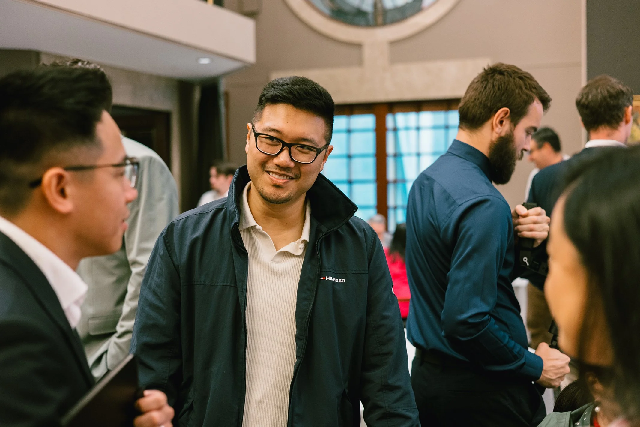 Group of people at a social gathering, engaging in conversation, with some smiling and others listening, indoors in a well-lit room.
