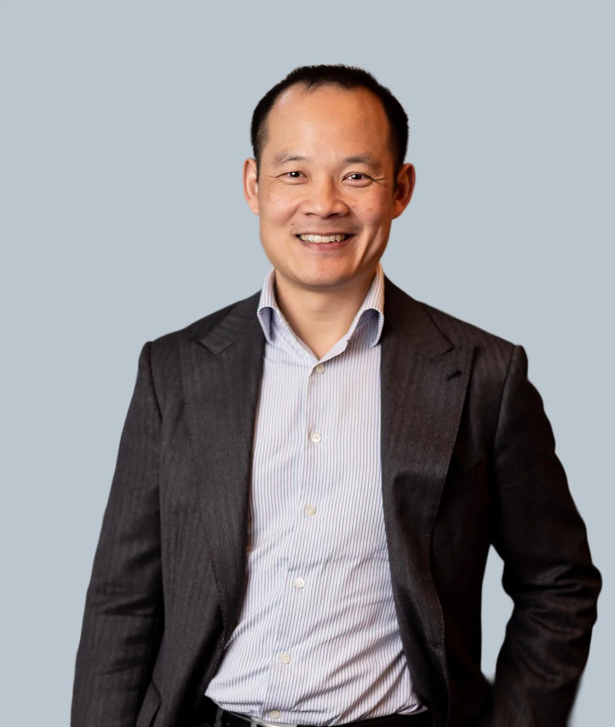 A confident man in a business suit smiles at the camera against a plain light blue background.