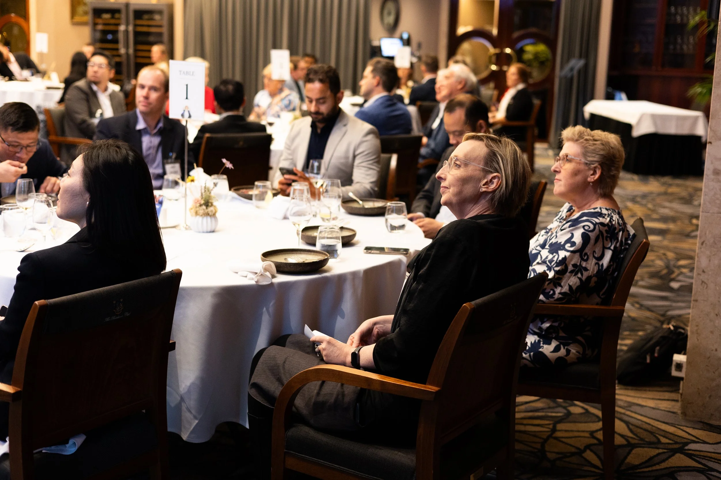 People attending a formal event seated around a table in a dimly lit banquet hall