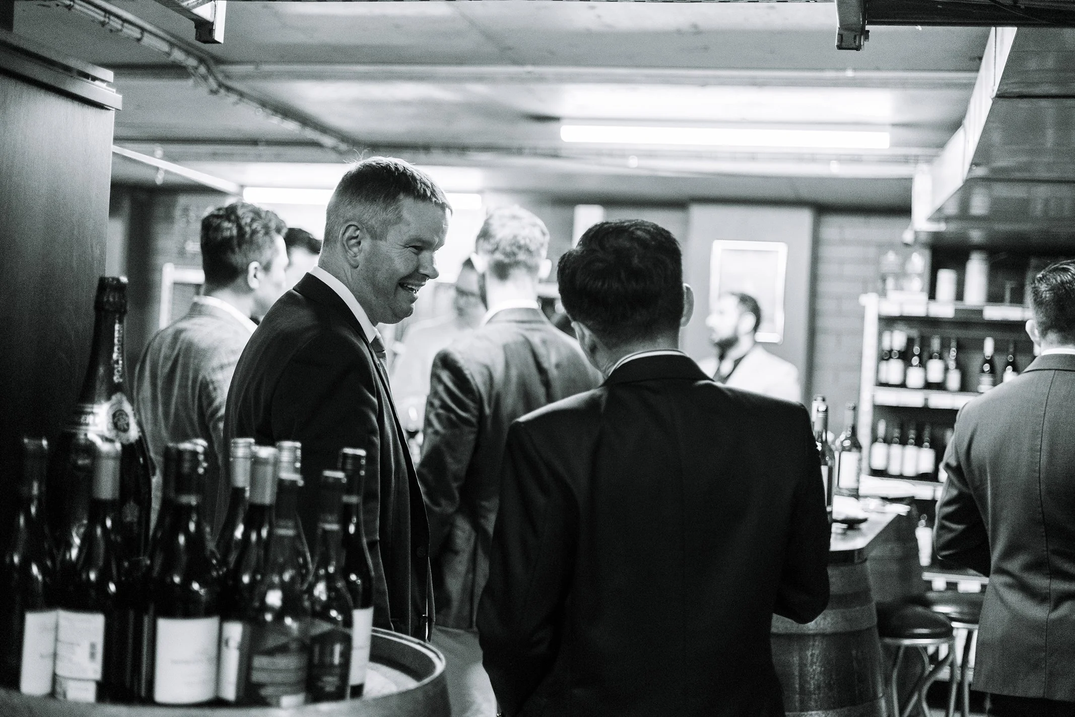 Group of men in suits socializing at a bar in a dimly lit setting.