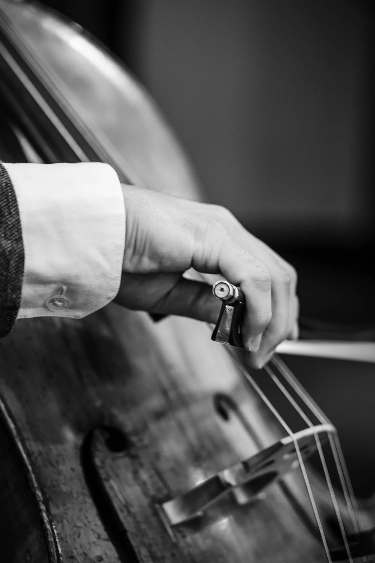 A black and white close-up of a person playing a guitar, focusing on their hand holding a guitar pick and the neck of the guitar.