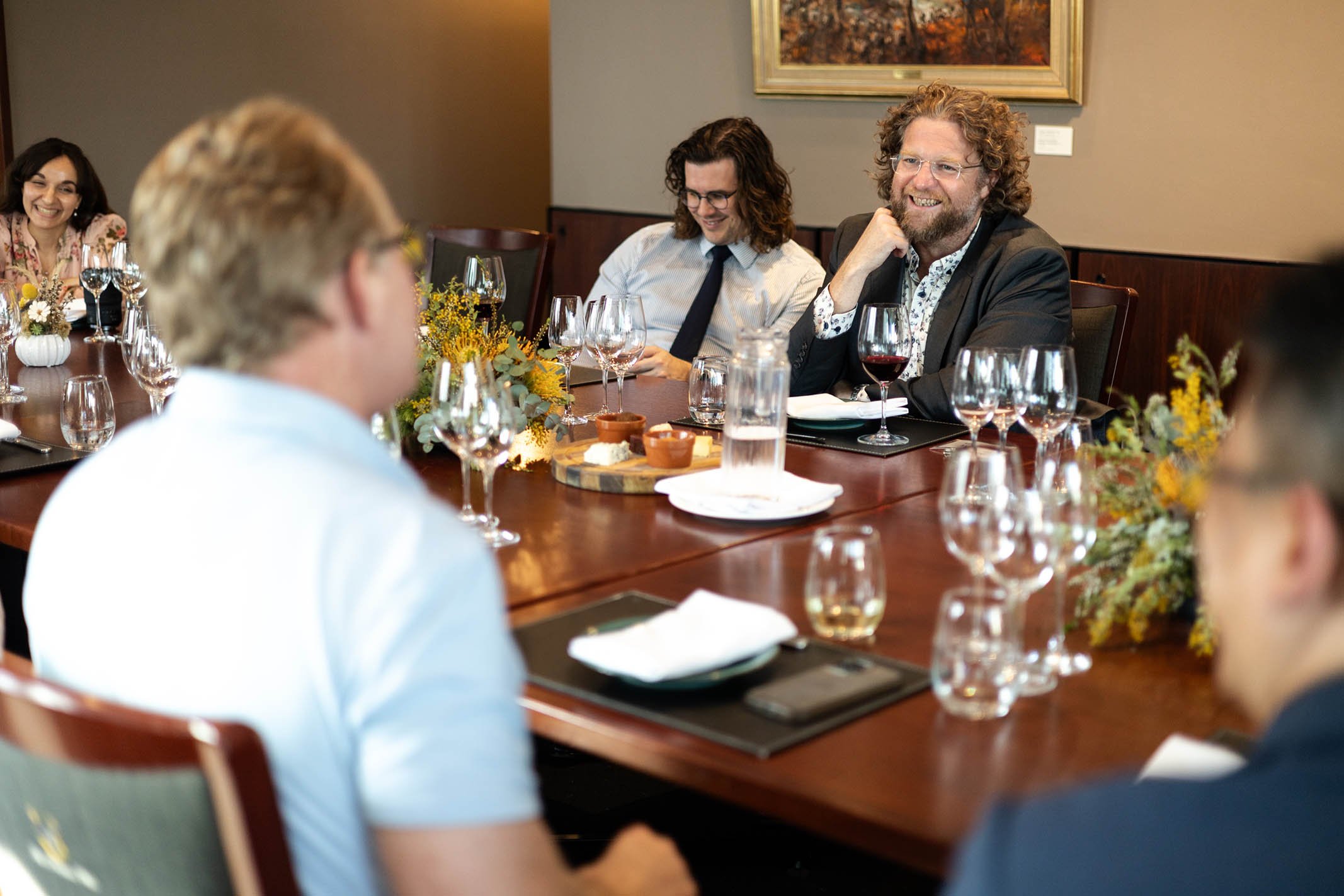 Group of people enjoying a dinner party at a formal dining table, with wine glasses, floral centerpieces, and appetizers.