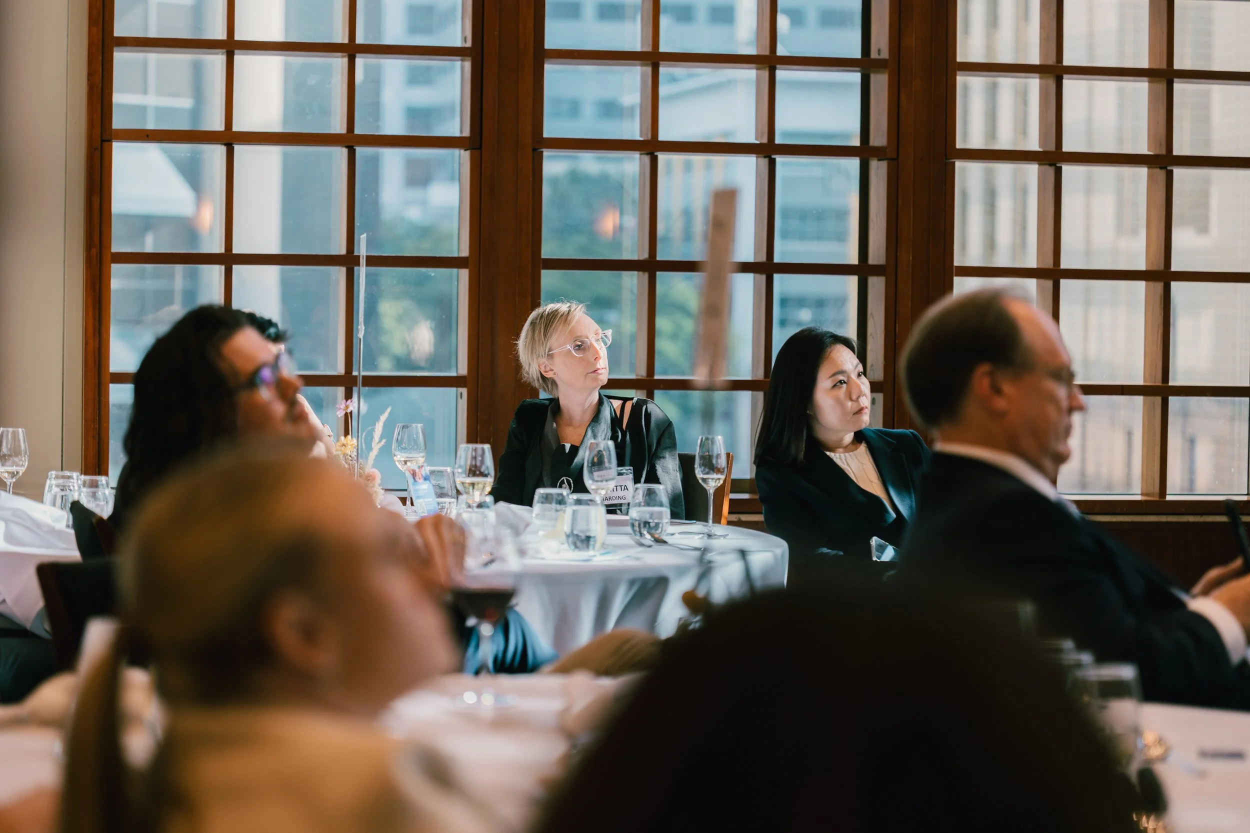 Attendees listening attentively at a conference or seminar in a room with large windows and wooden framing.