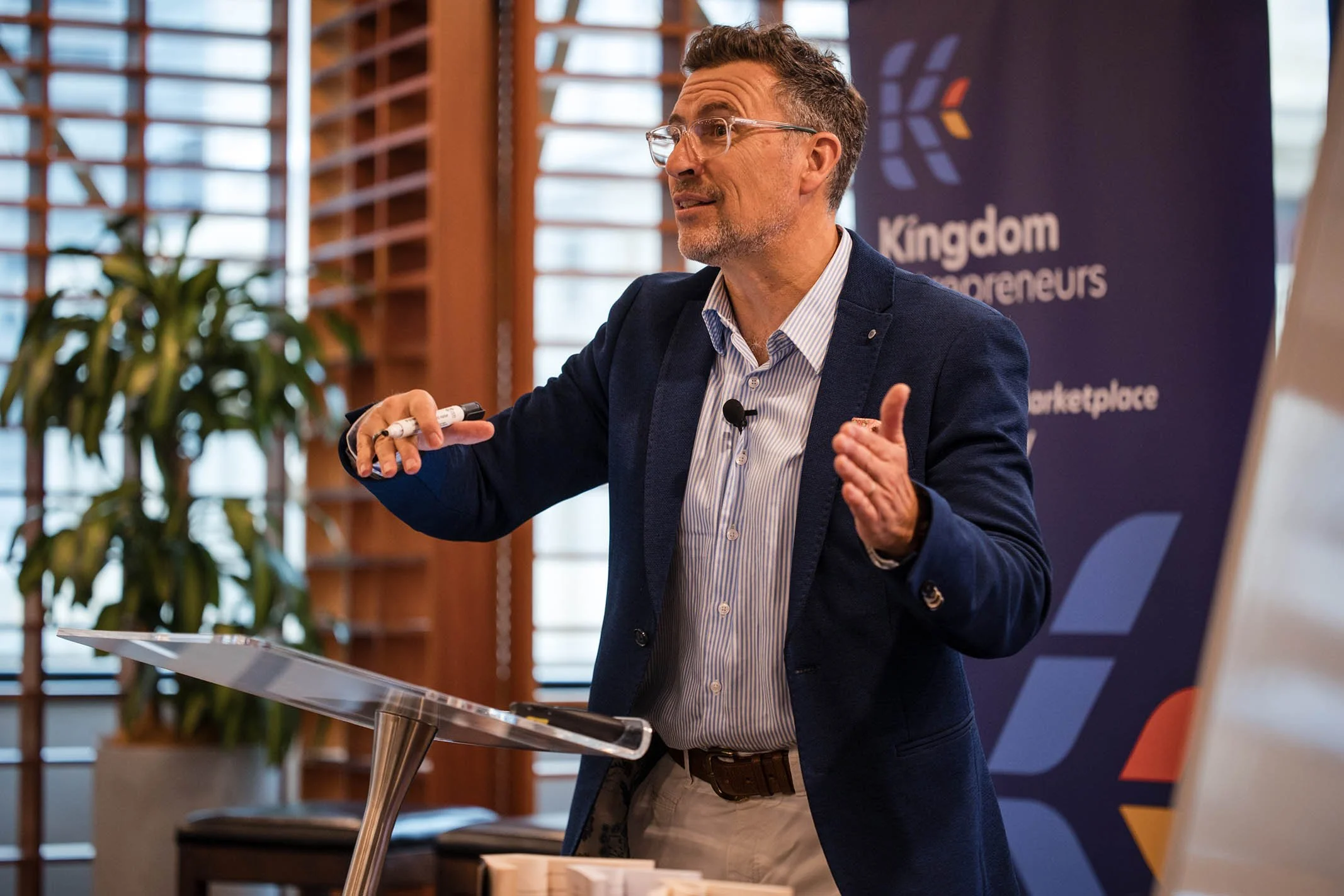 A man giving a presentation in a conference room with a Kingdom Entrepreneurs banner in the background.