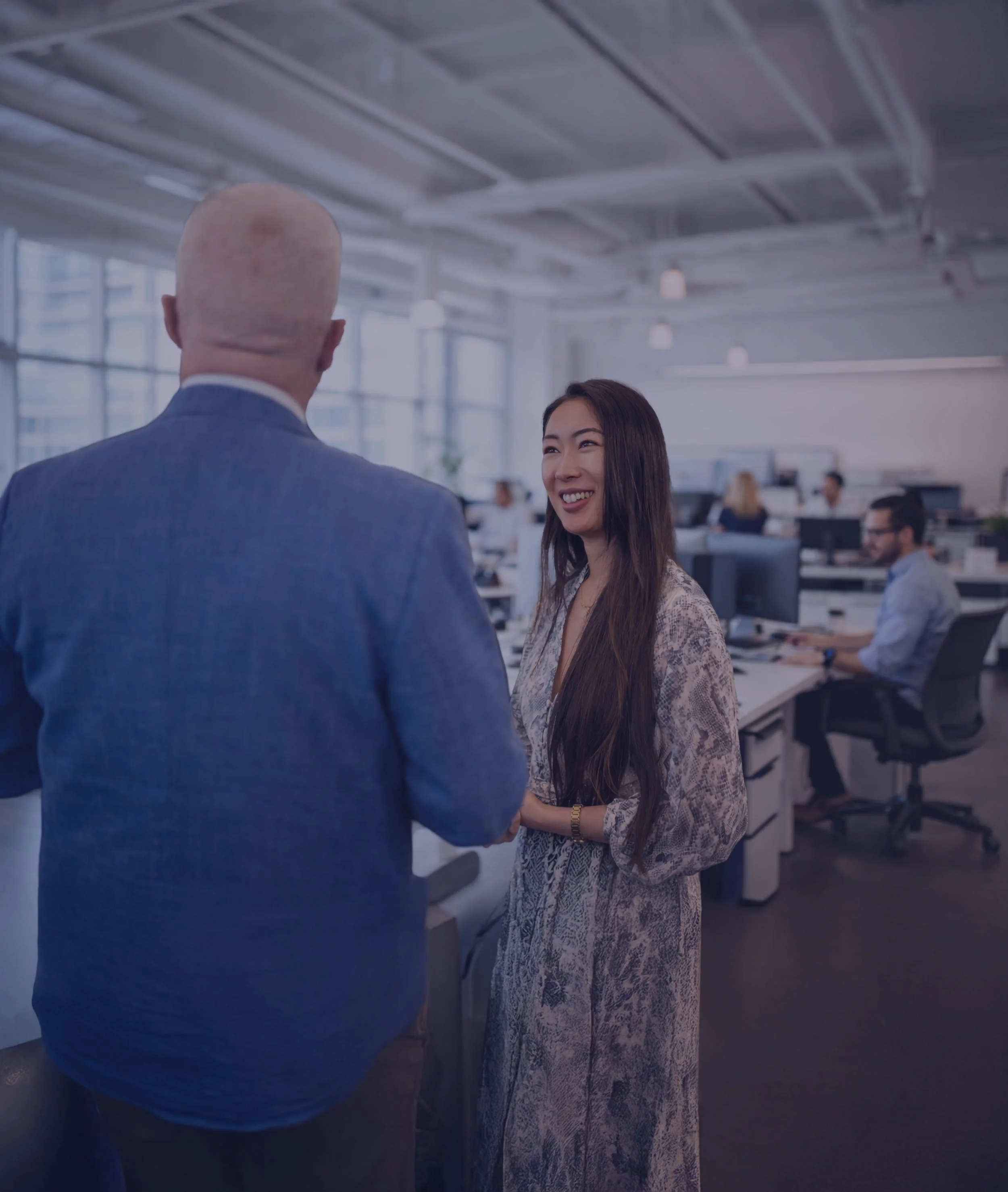 Professional woman smiling and talking with a colleague in a modern open-plan office environment