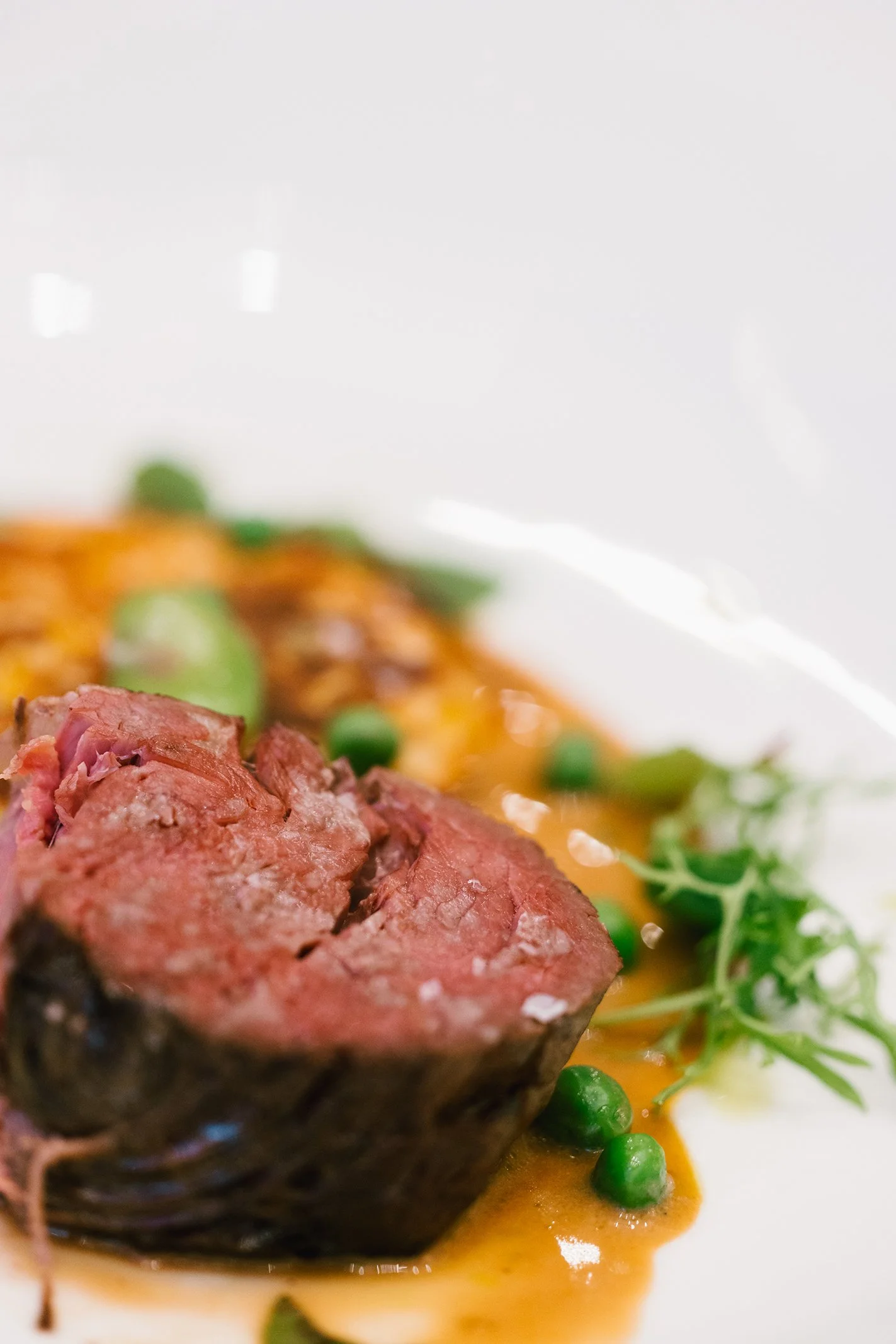 Close-up of a medium-rare beef tenderloin steak with green peas, sauce, and garnish on a white plate.