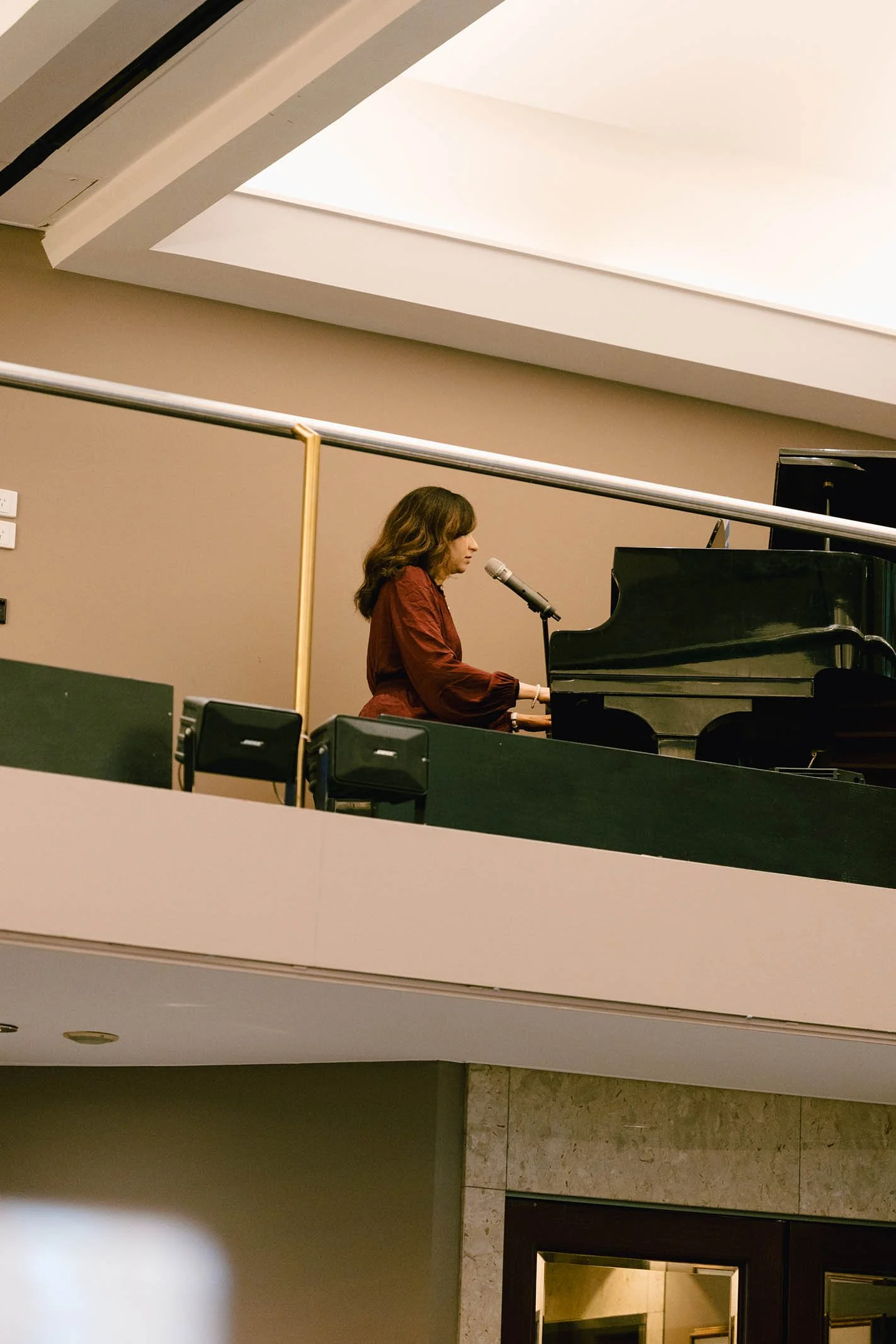 A woman is playing the piano and singing into a microphone in an indoor setting.