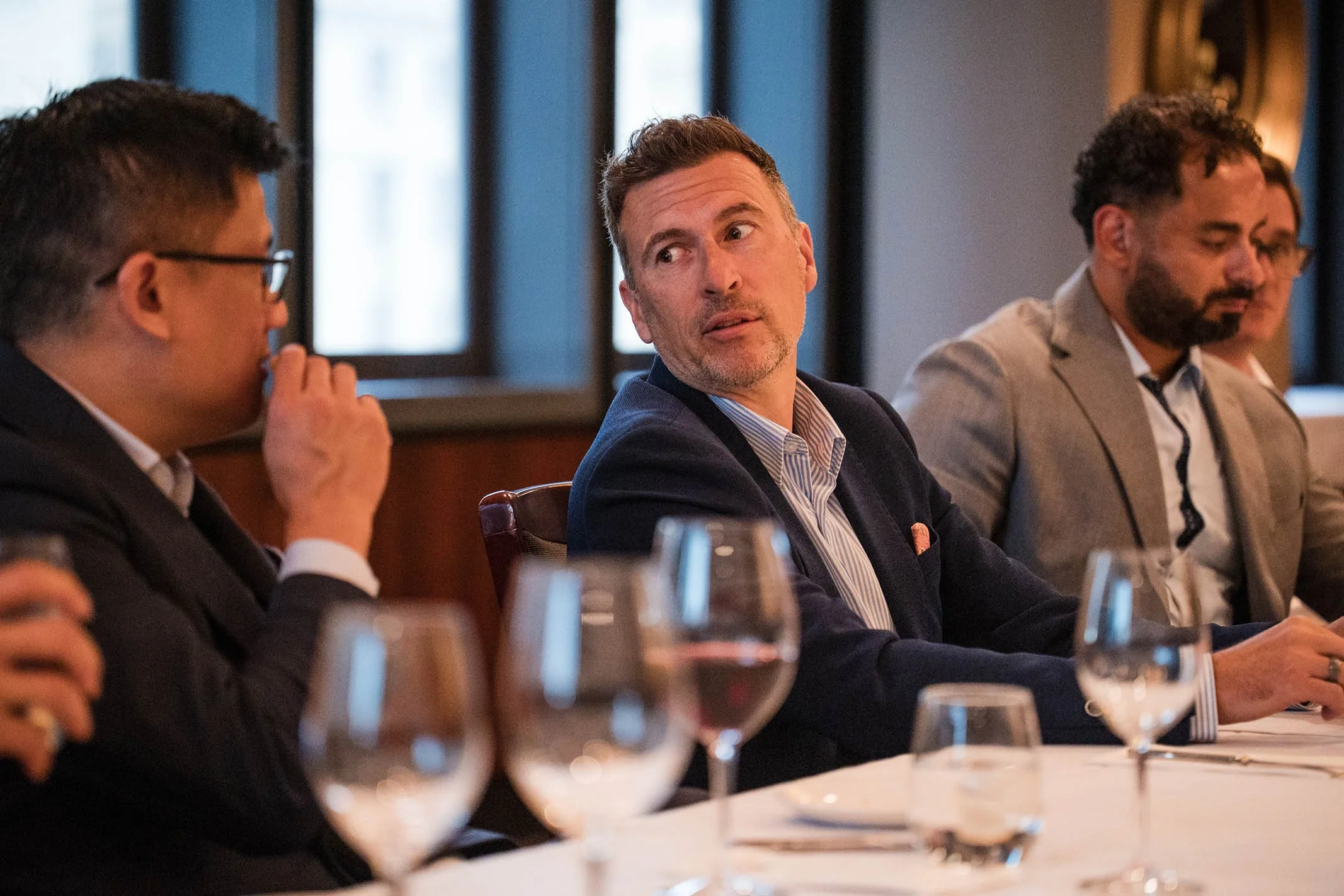 People sitting at a conference table, engaged in a discussion, with glasses of water in front of them.