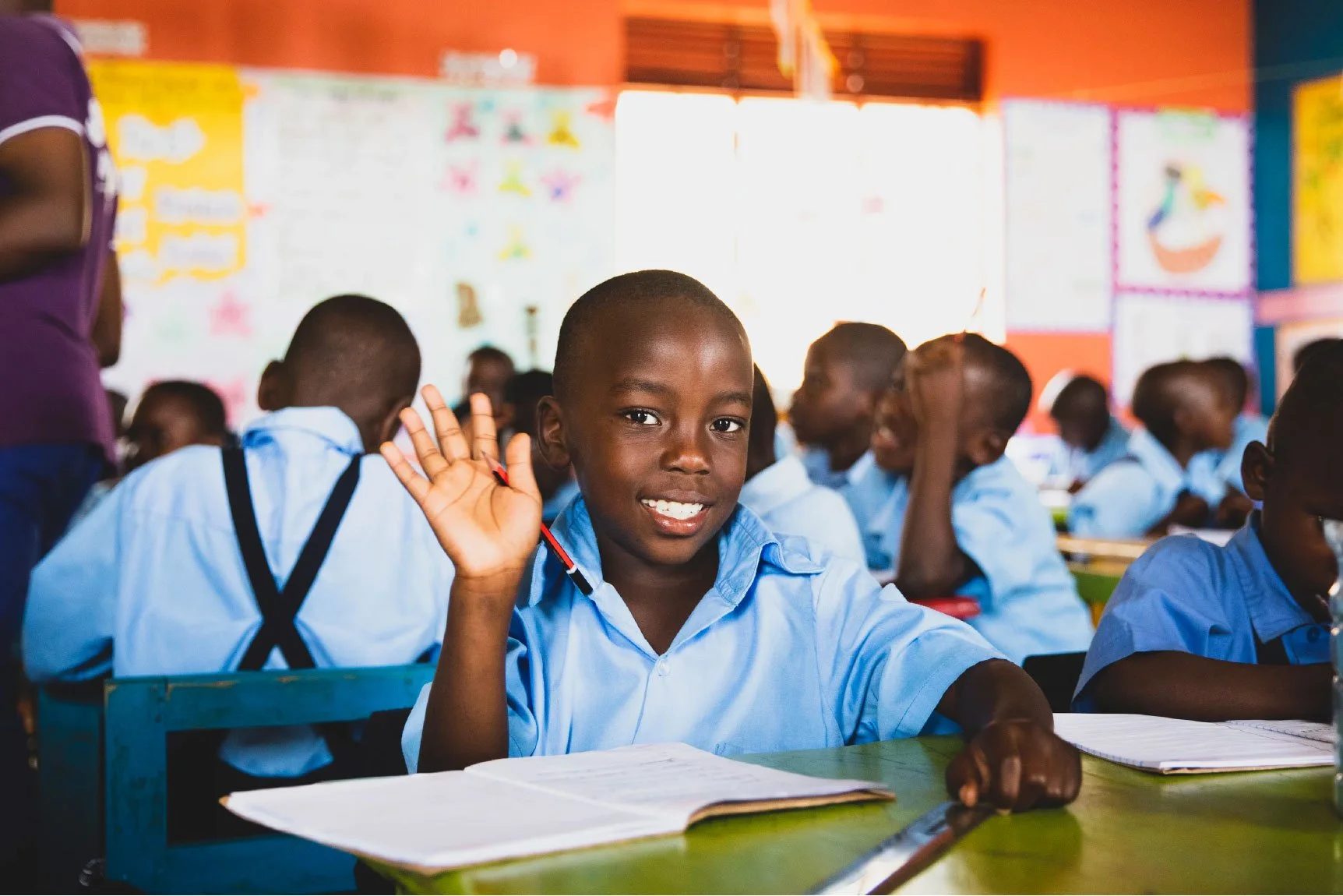 Student smiling and raising a hand in a classroom in Uganda