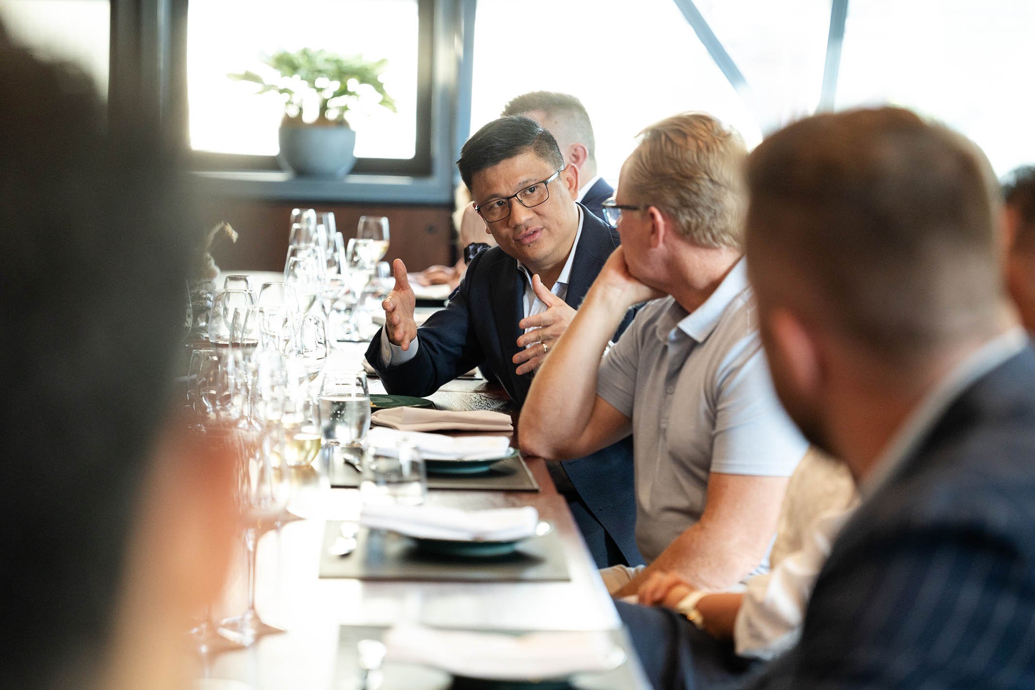People sitting at a long dining table engaged in conversation during a formal meeting or discussion.