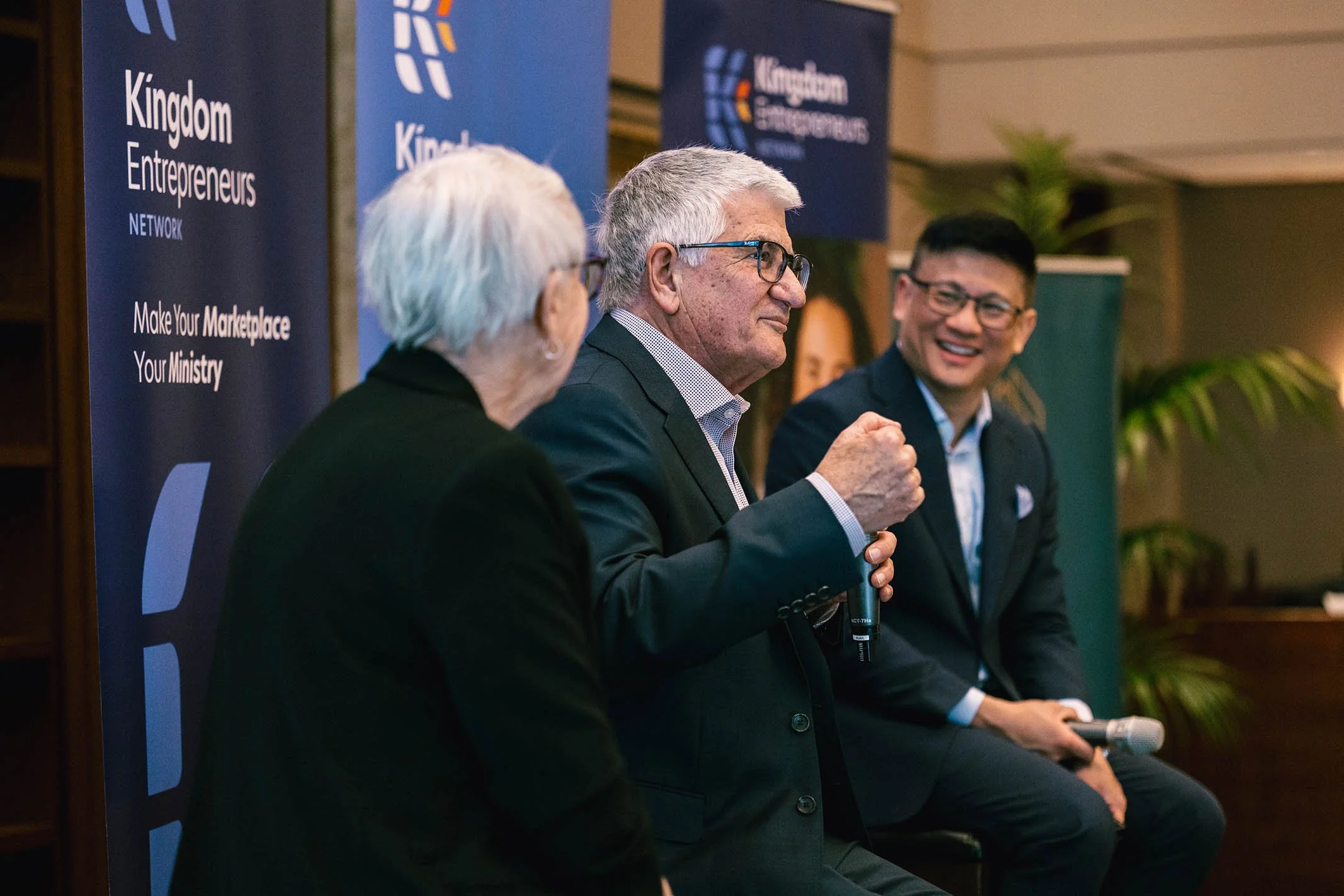 Three people sitting and speaking at a panel or conference event, with banners in the background that read 'Kingdom Entrepreneurs Network' and 'Make Your Marketplace, Your Ministry.'