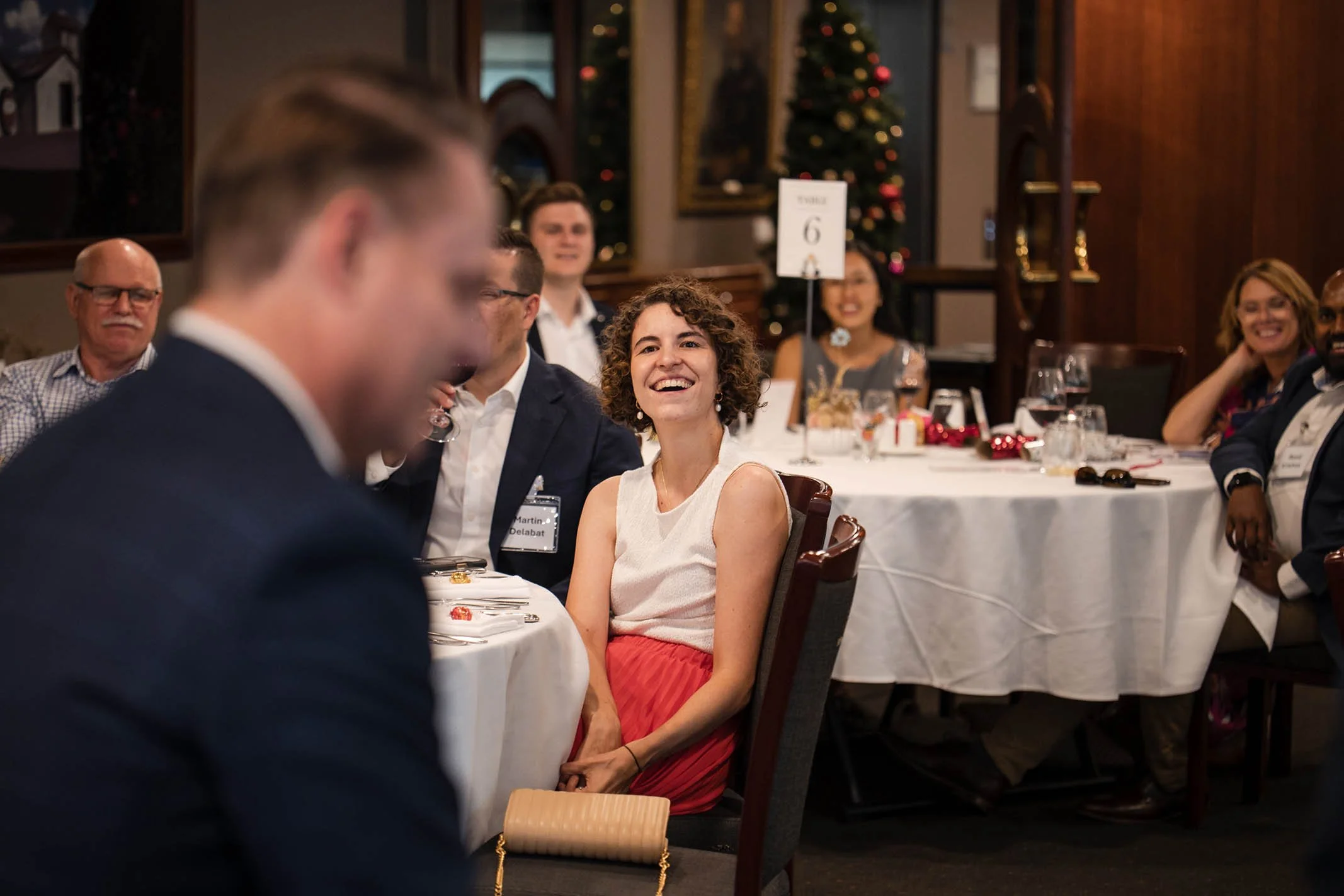 People sitting at a banquet table during a Christmas celebration, with a decorated Christmas tree in the background.
