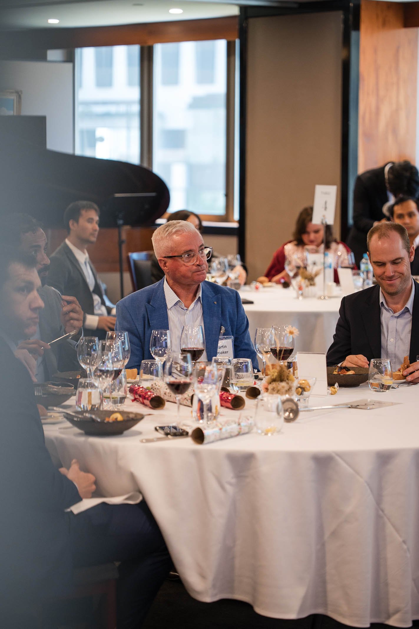 People sitting at a round table during a formal event, with Christmas decorations and wine glasses on the table.
