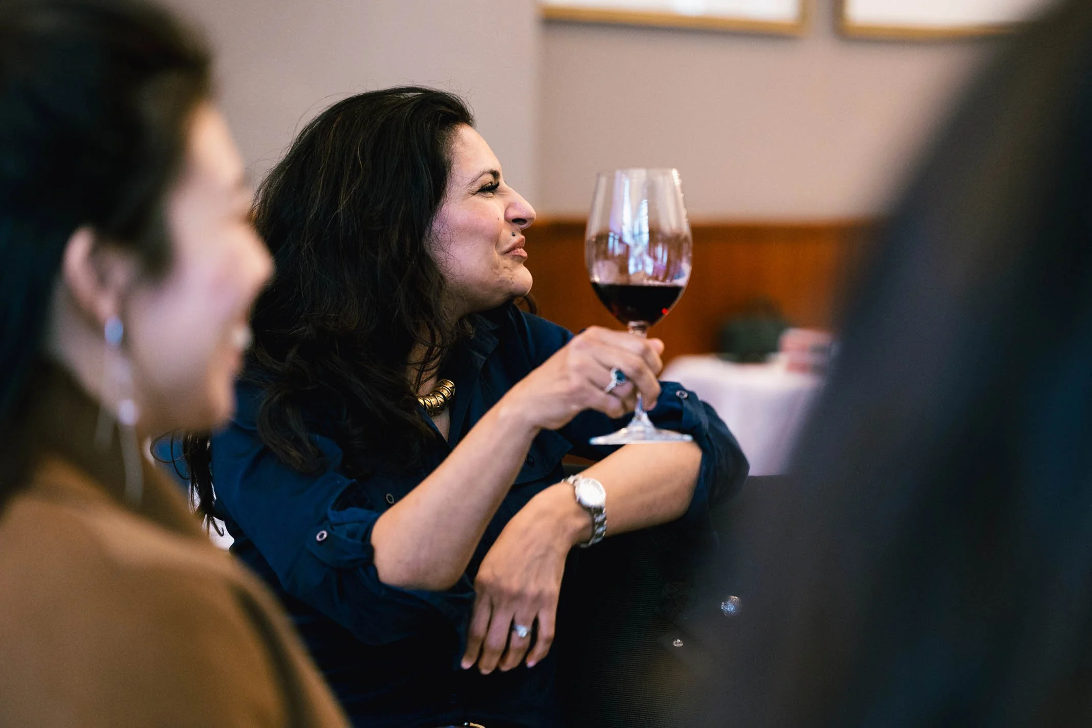 Woman with dark curly hair holding a glass of red wine at a social gathering.