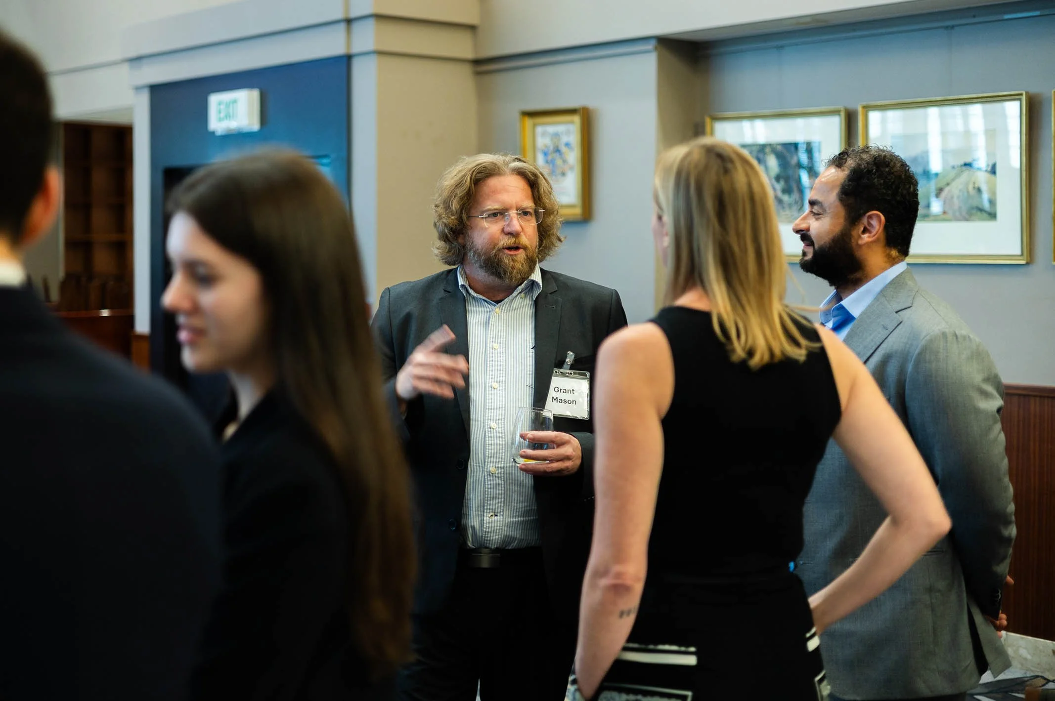 Group of professionals at a networking event engaged in conversation, with framed artwork on the walls in the background.