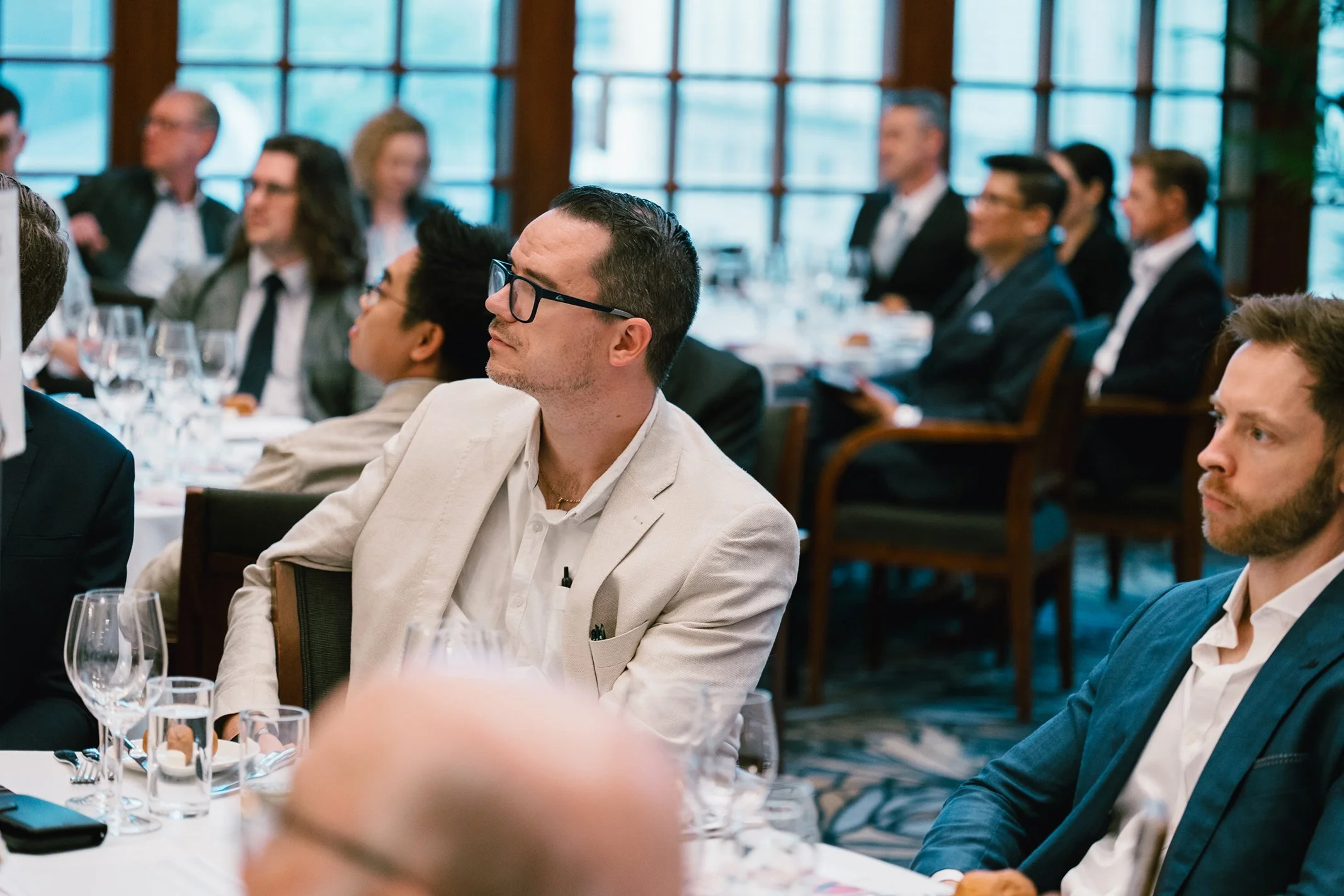 Business professionals attending a conference or meeting in a formal setting with large windows and natural light.