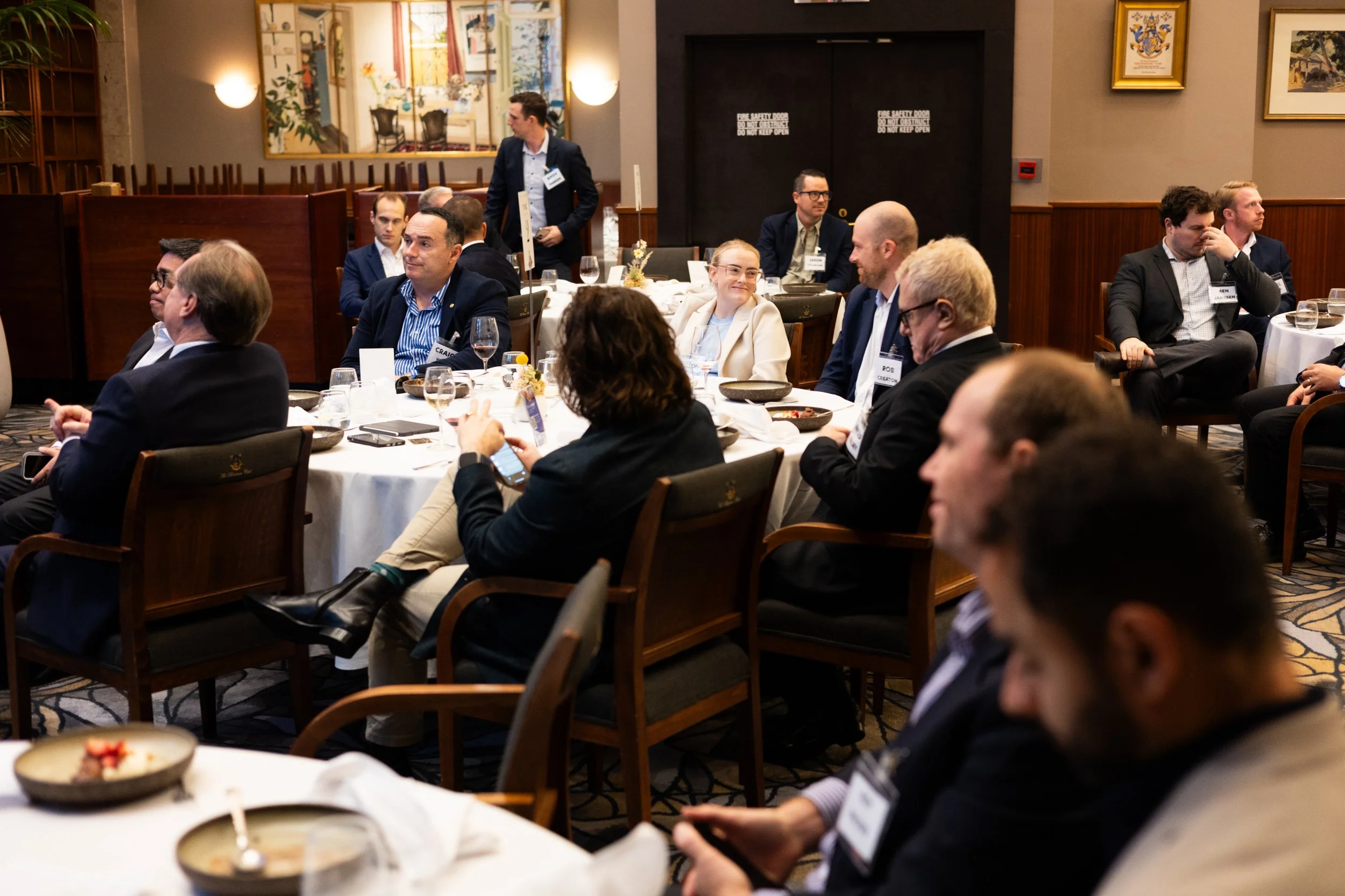 Business professionals seated at round tables in a conference room, participating in a formal meeting or presentation.