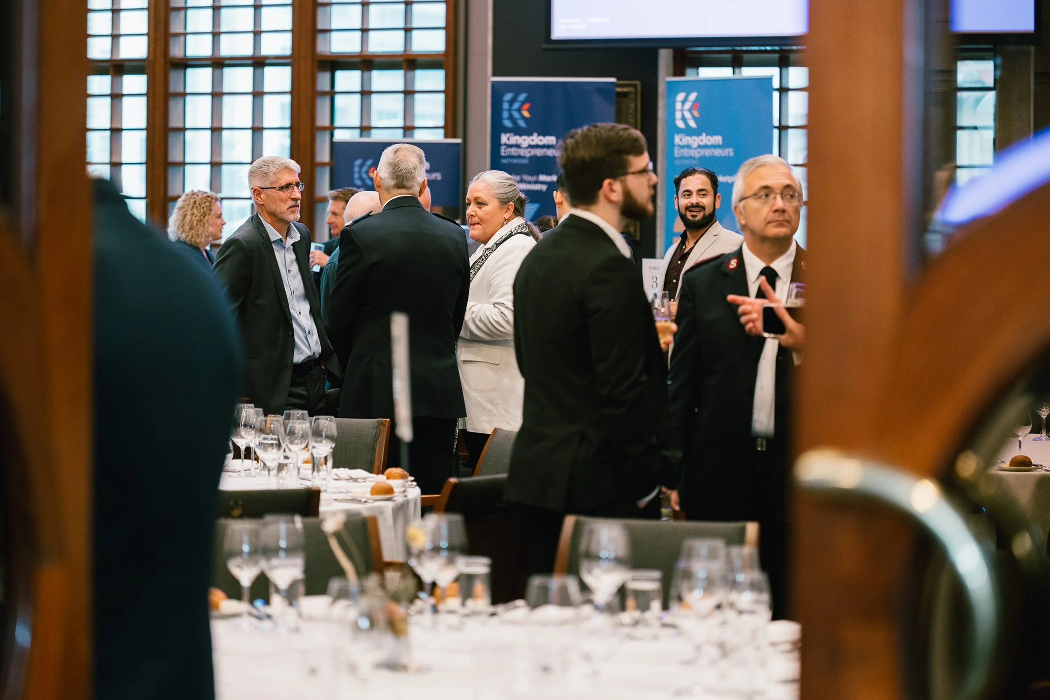 People in formal attire mingling at a professional networking event or conference with banners reading 'Kingdom Entrepreneurs' in the background.