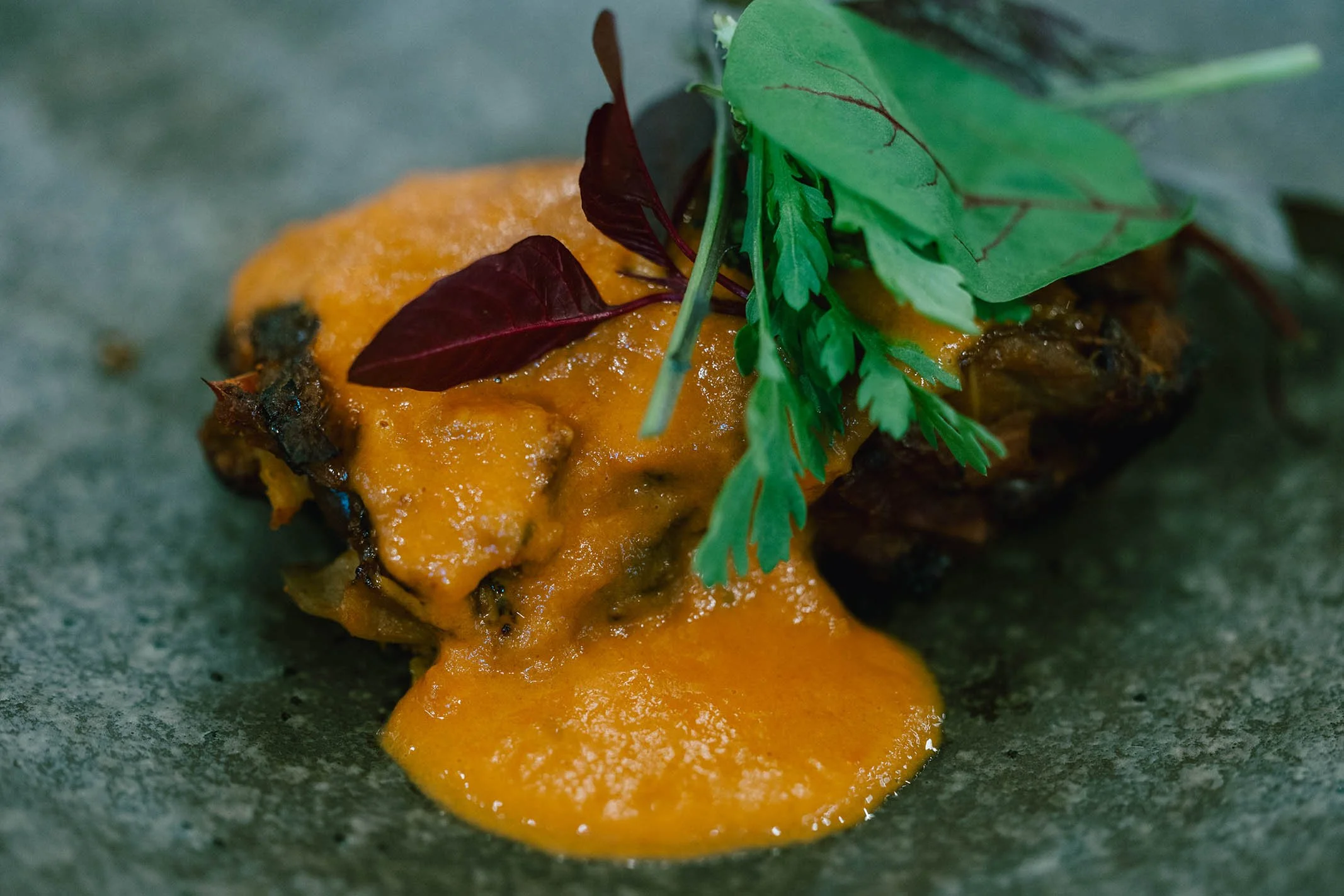 A close-up of a food item with melted cheese and garnished with fresh green herbs on it.