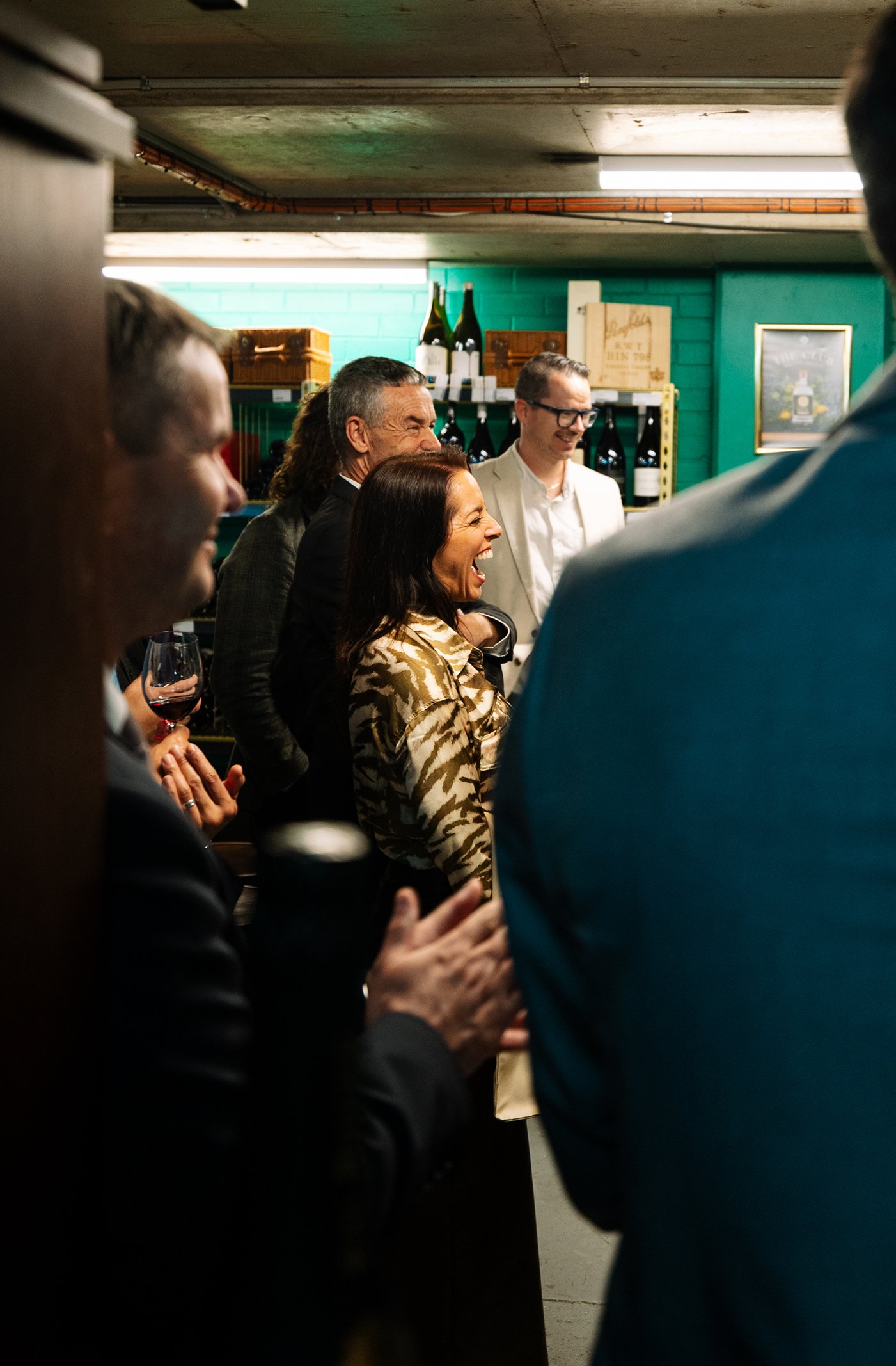 Group of people laughing and enjoying a social gathering in a bar or cellar setting.