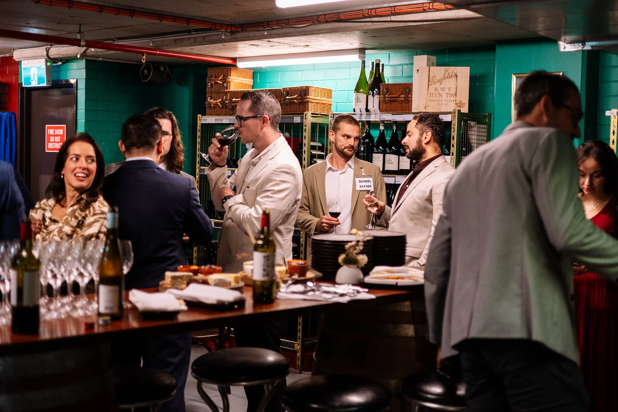 People at a social gathering in a bar or wine lounge, with wine bottles and glasses, in a cozy and stylish setting.