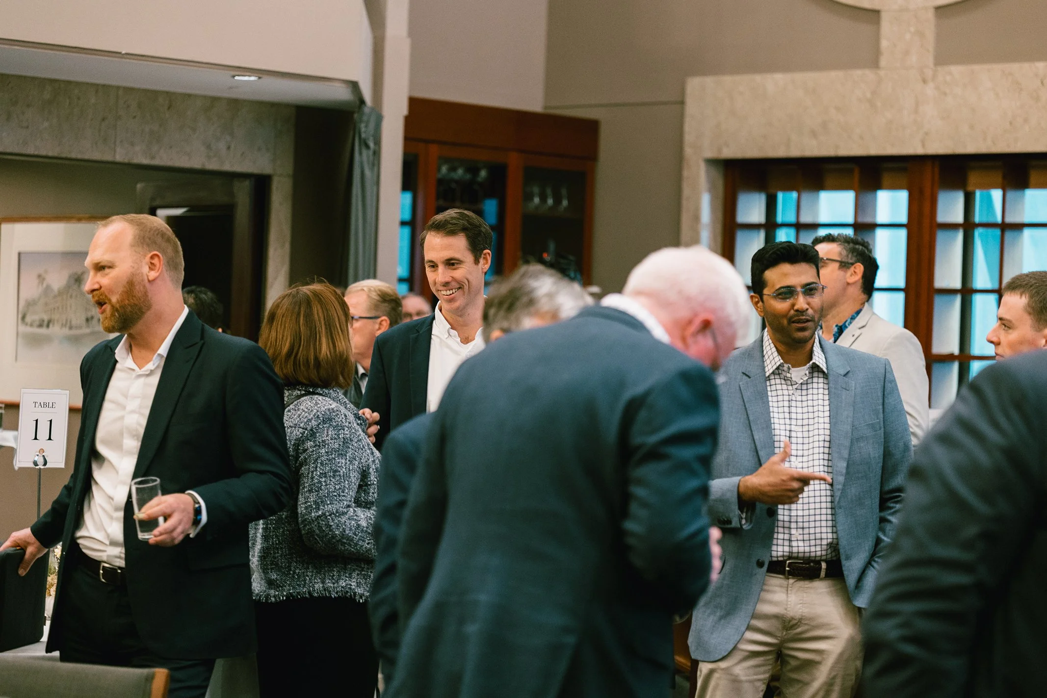 Business professionals socializing at a formal event in a conference room, dressed in suits and business attire, engaging in conversations.