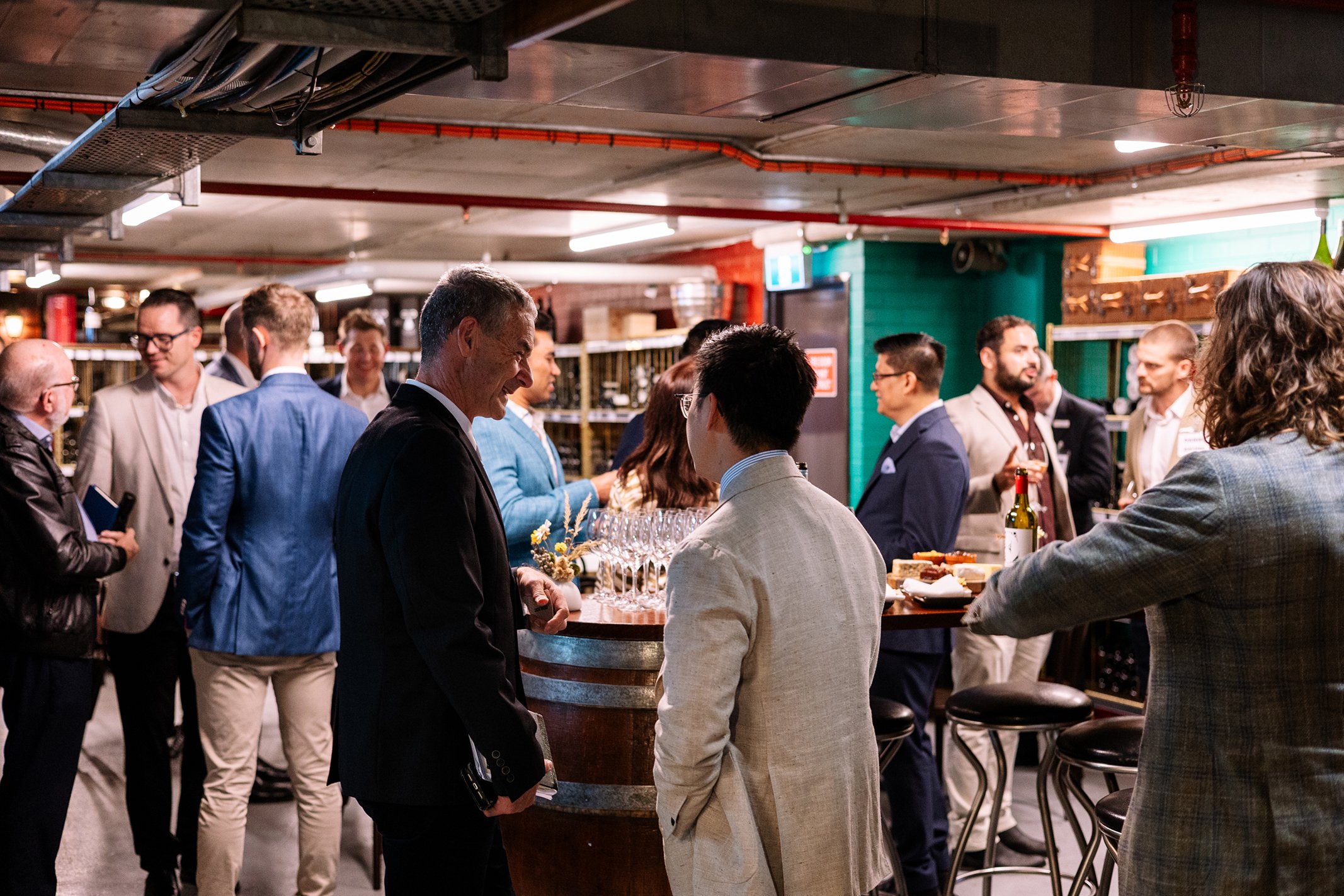 People socializing at a bar or event space with wine bottles and glasses on the counter.