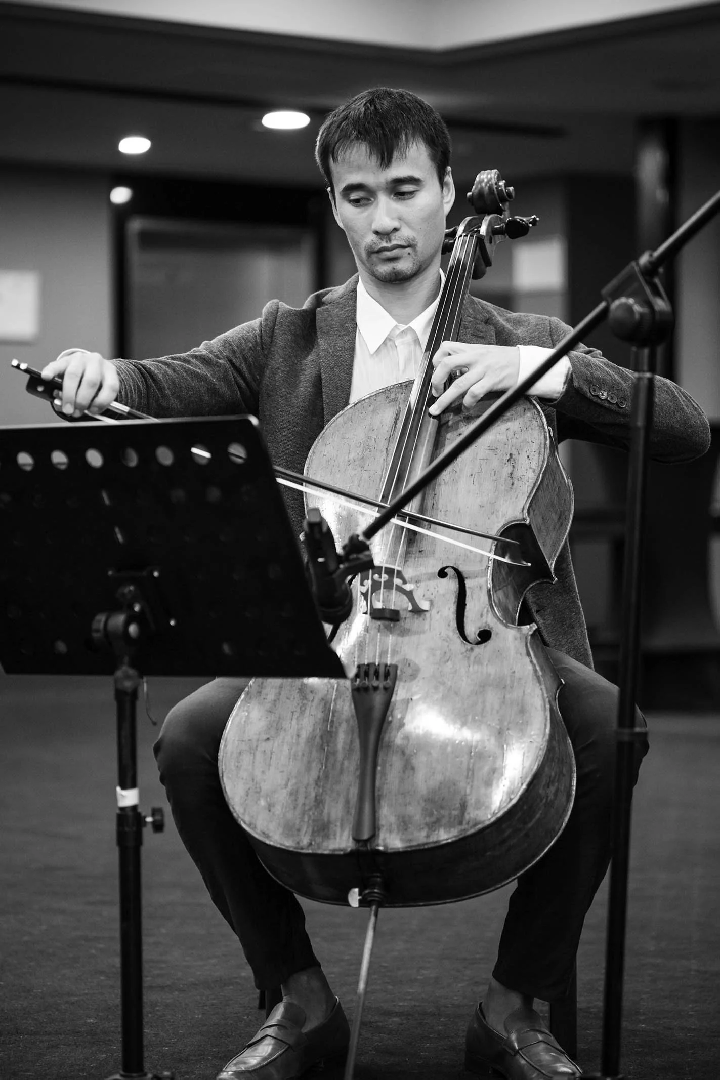 A man in formal attire playing a cello during a recording session in a studio.