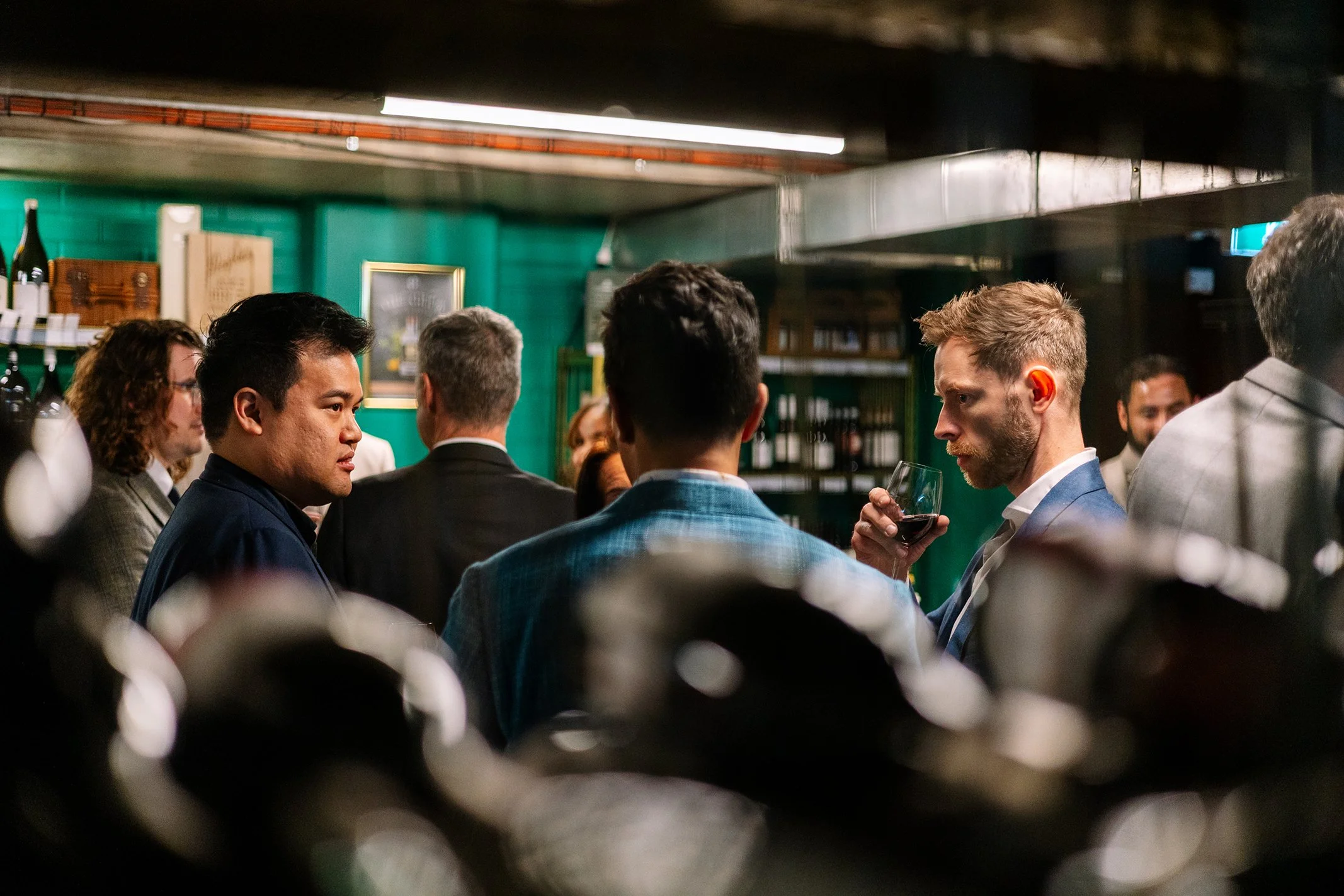 People socializing in a bar, with a man drinking red wine in focus.