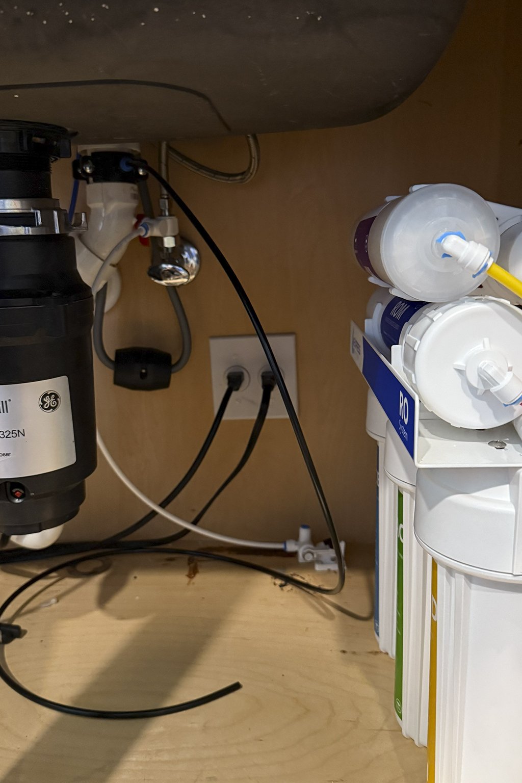 Under-sink water filtration system with cartridges and plumbing connections.