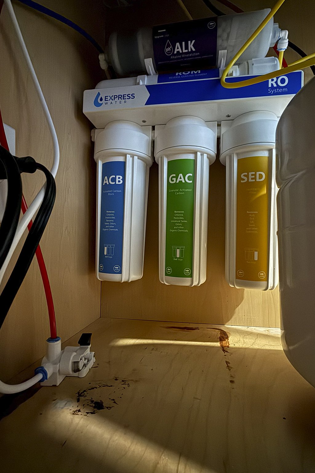 A water filtration system with three filters labeled ACB, GAC, and SED, mounted under the sink with various pipes and tubes connected.