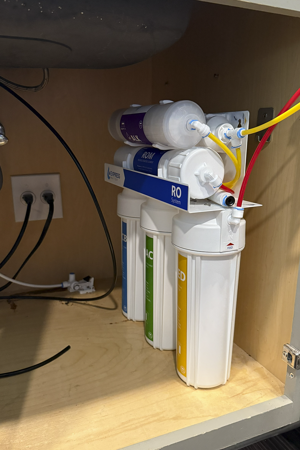 Under sink water filtration system with multiple filter cartridges installed inside a wooden cabinet.