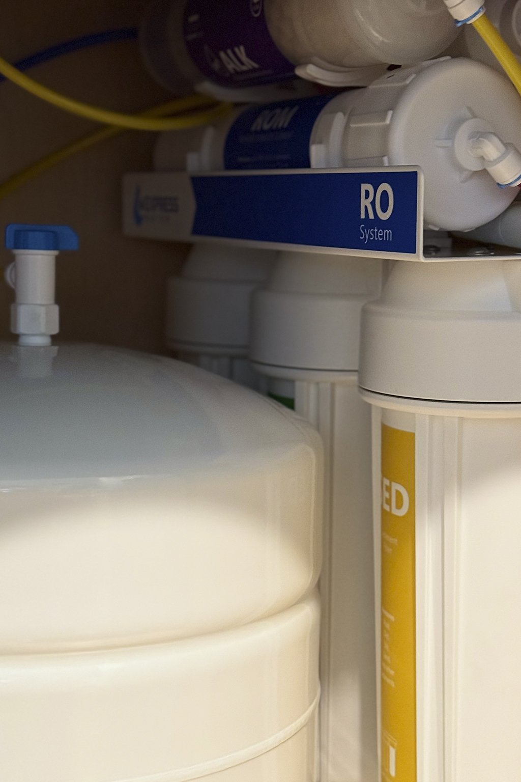 A reverse osmosis (RO) water filtration system installed in a water supply setup, with various filters and tubing visible.