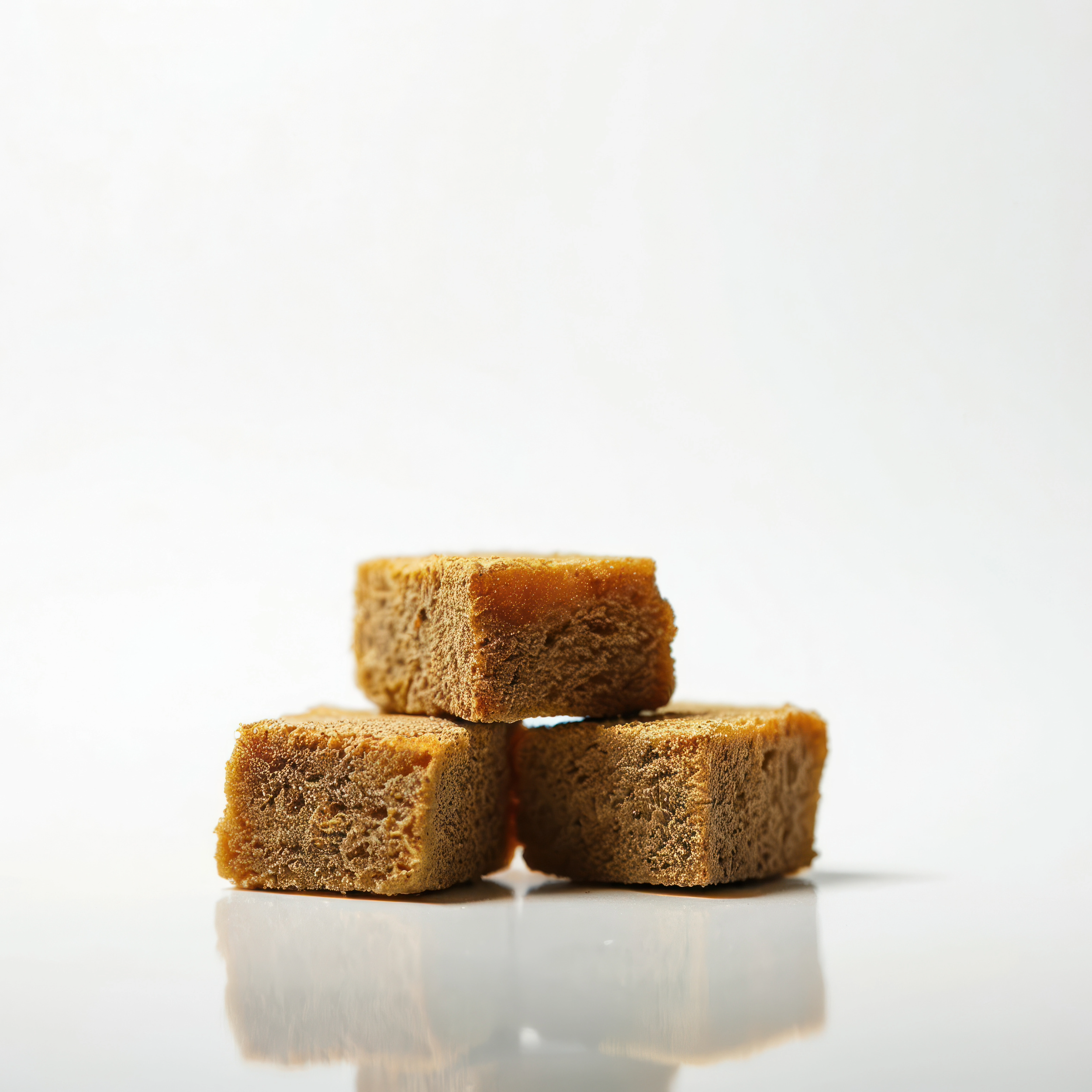 Three brown sugar cubes stacked on a white surface against a plain white background.