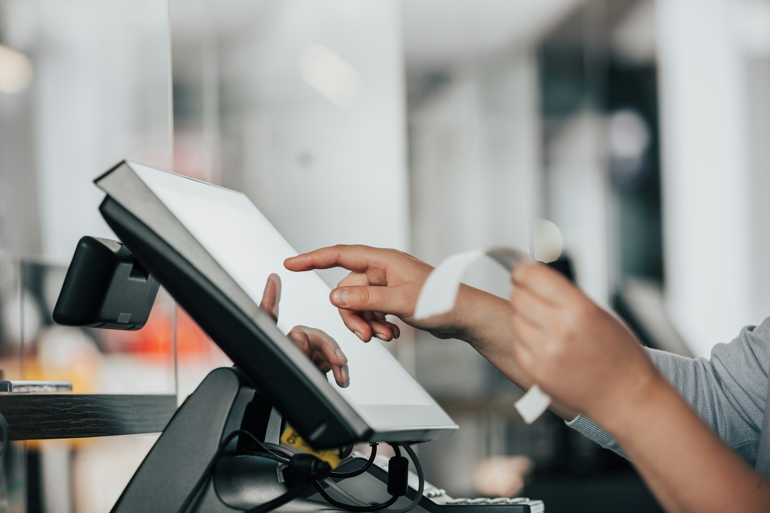 Person using a touchscreen register and holding a credit card at a checkout counter.